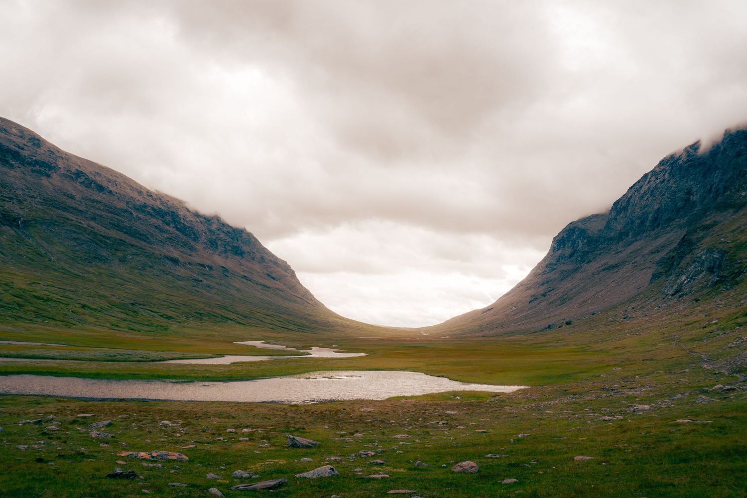 A serene glacial valley with small lakes nestled between two mountains under overcast skies.