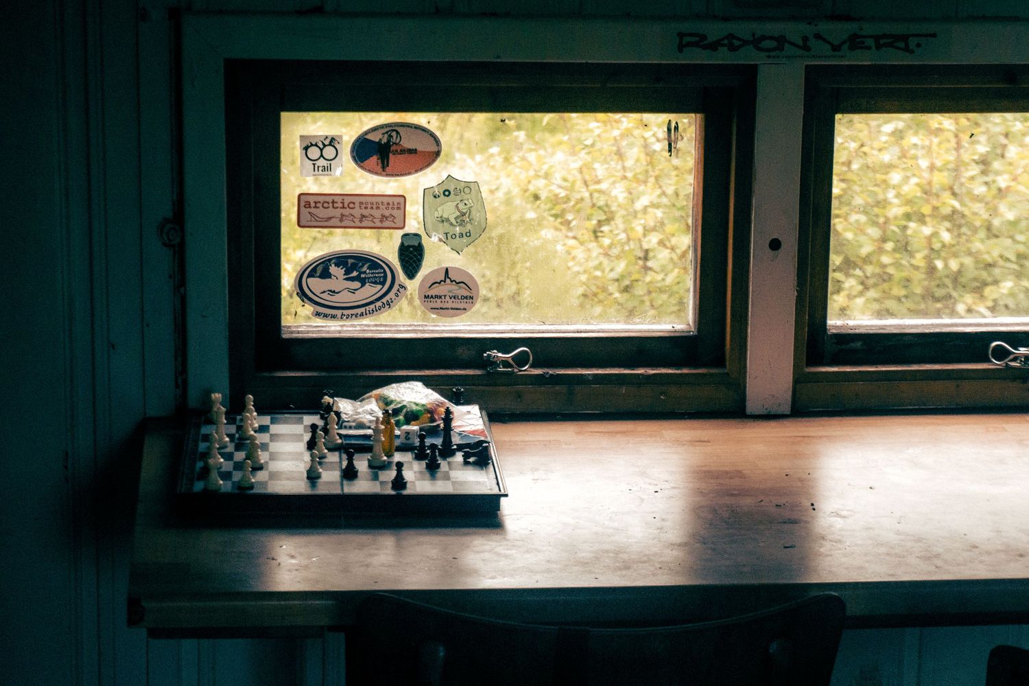 Chess board on wooden table near a window decorated with travel stickers in a cabin.