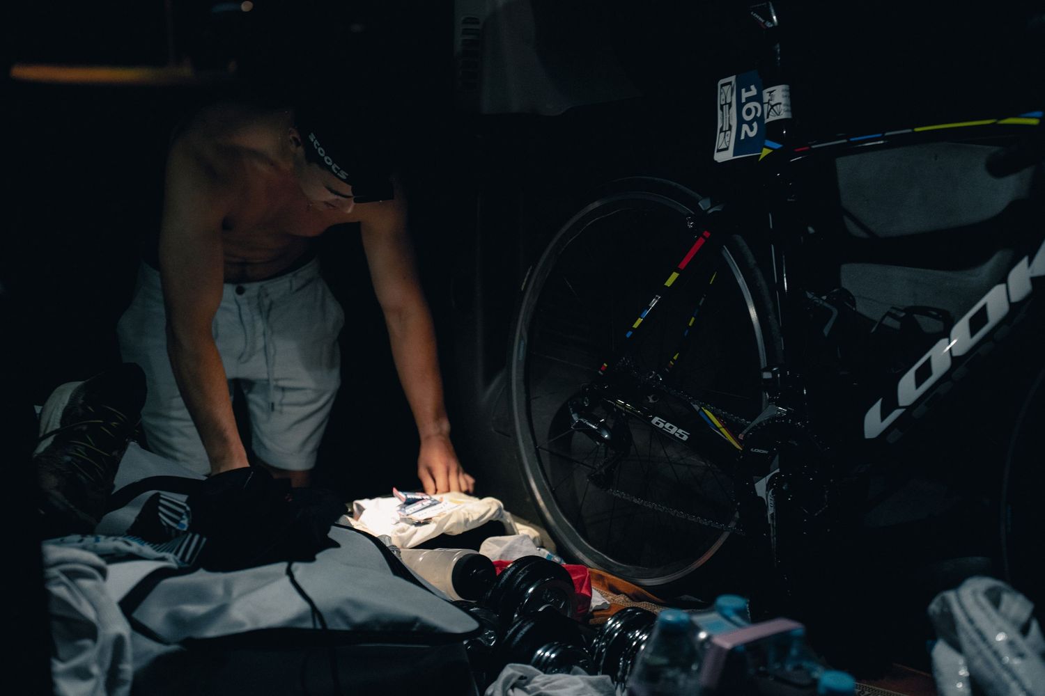 Cyclist preparing gear in dark transition area with a Look road bike in the background during a triathlon event.