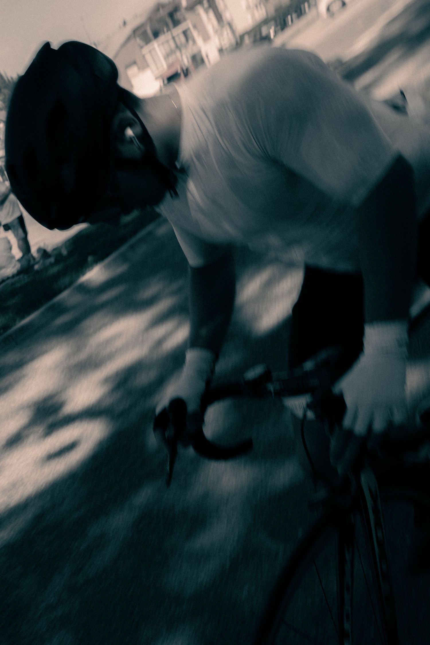 Black and white motion blur photo of a cyclist wearing a helmet riding a road bike at high speed.