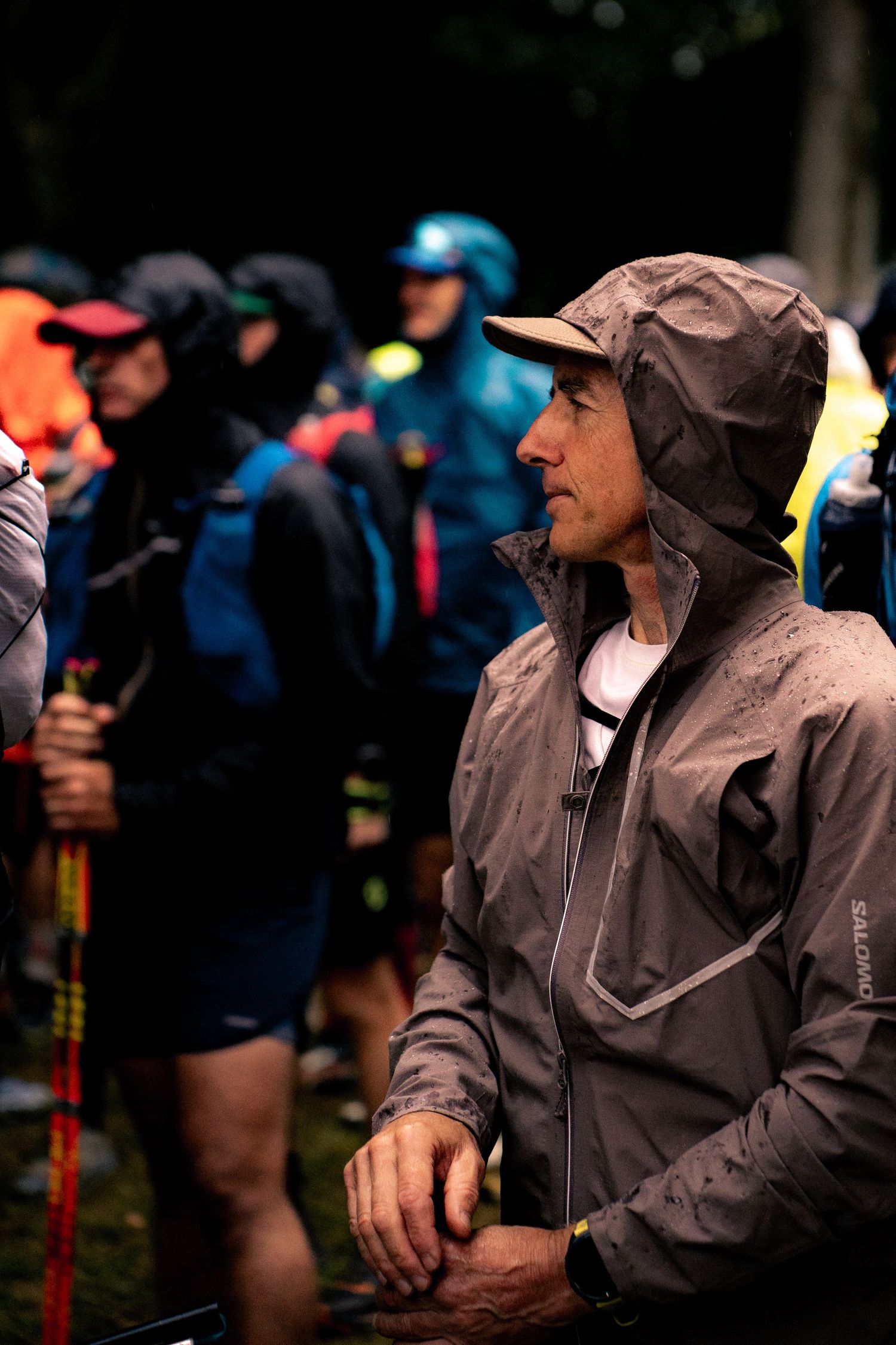 Trail runner in gray Salomon rain jacket with hood up at rainy race start.