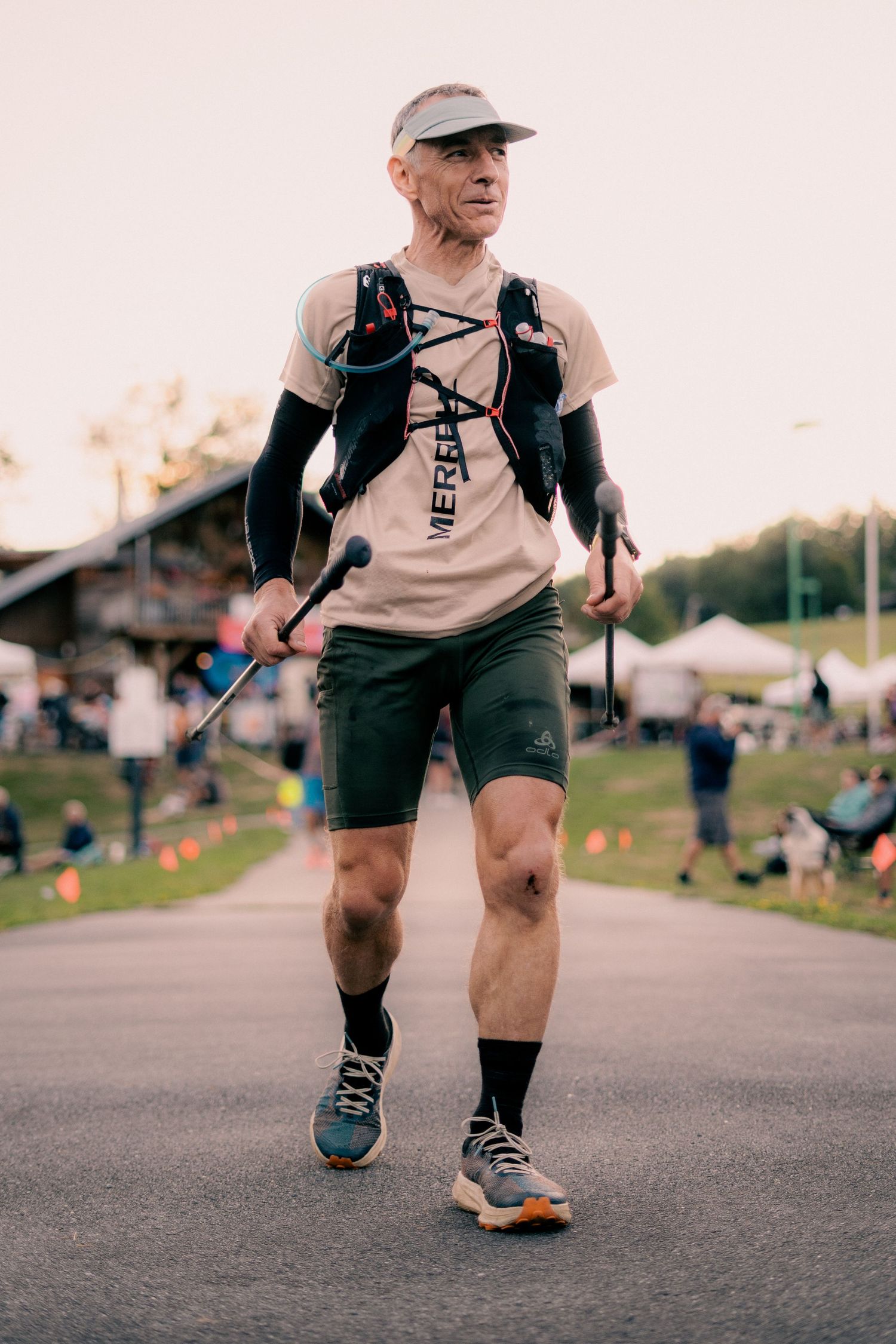 Determined male trail runner with hiking poles and a hydration vest walking on a path at dusk.
