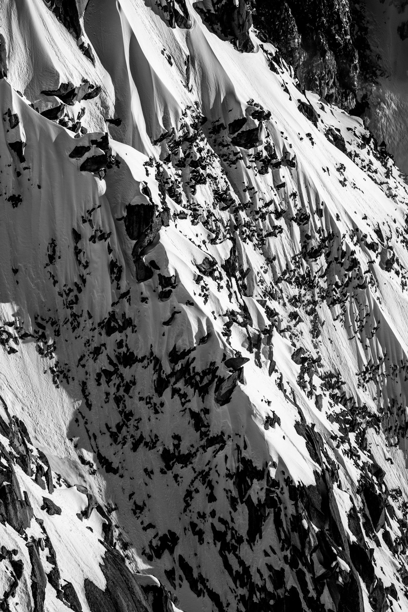 Black and white abstract texture of snow-draped rocky mountain cliffs with dramatic light and shadow contrast.