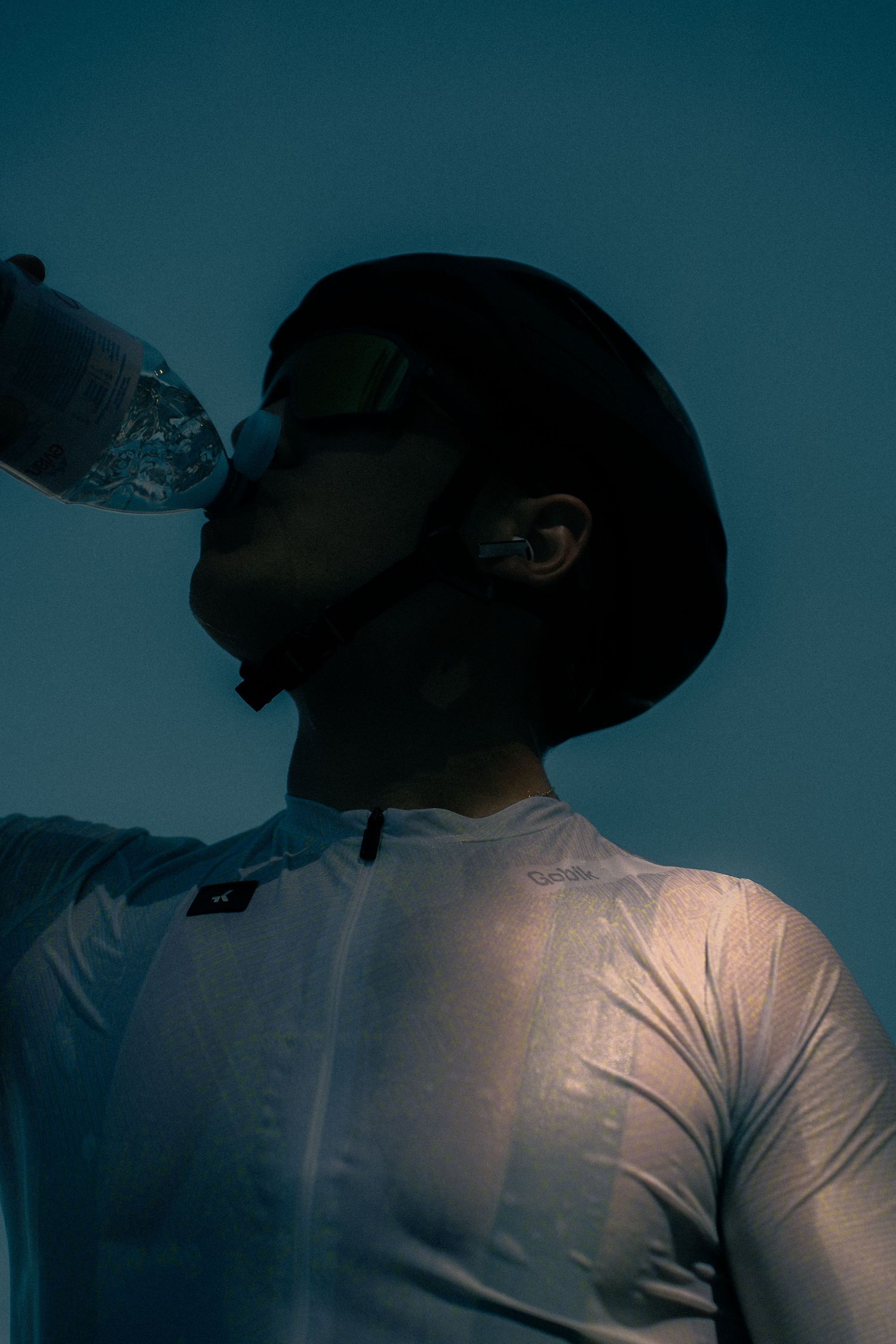 Man in white athletic shirt drinking from water bottle under dramatic blue lighting.