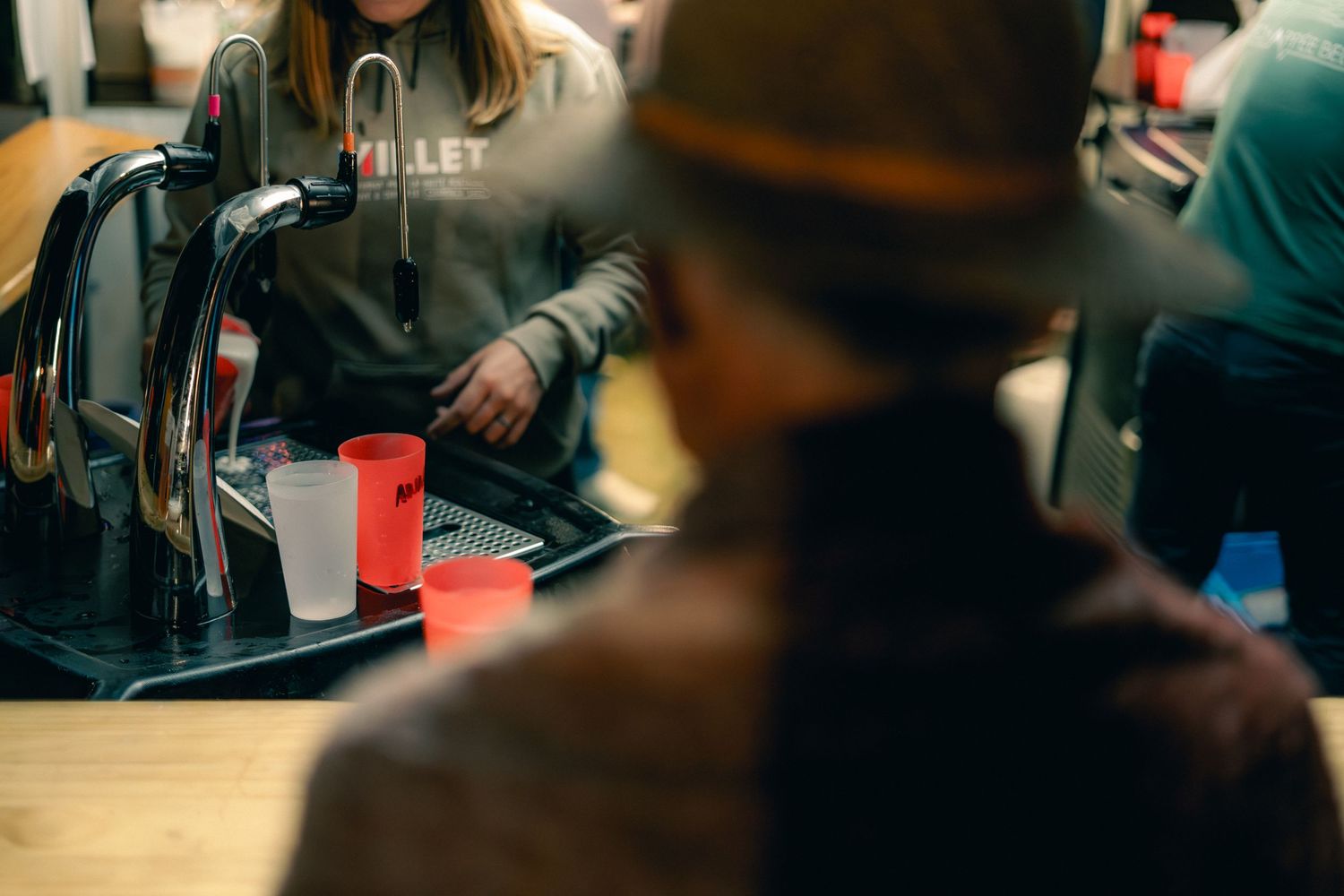 Race aid station volunteer filling cups at a Millet-branded refreshment table indoors.