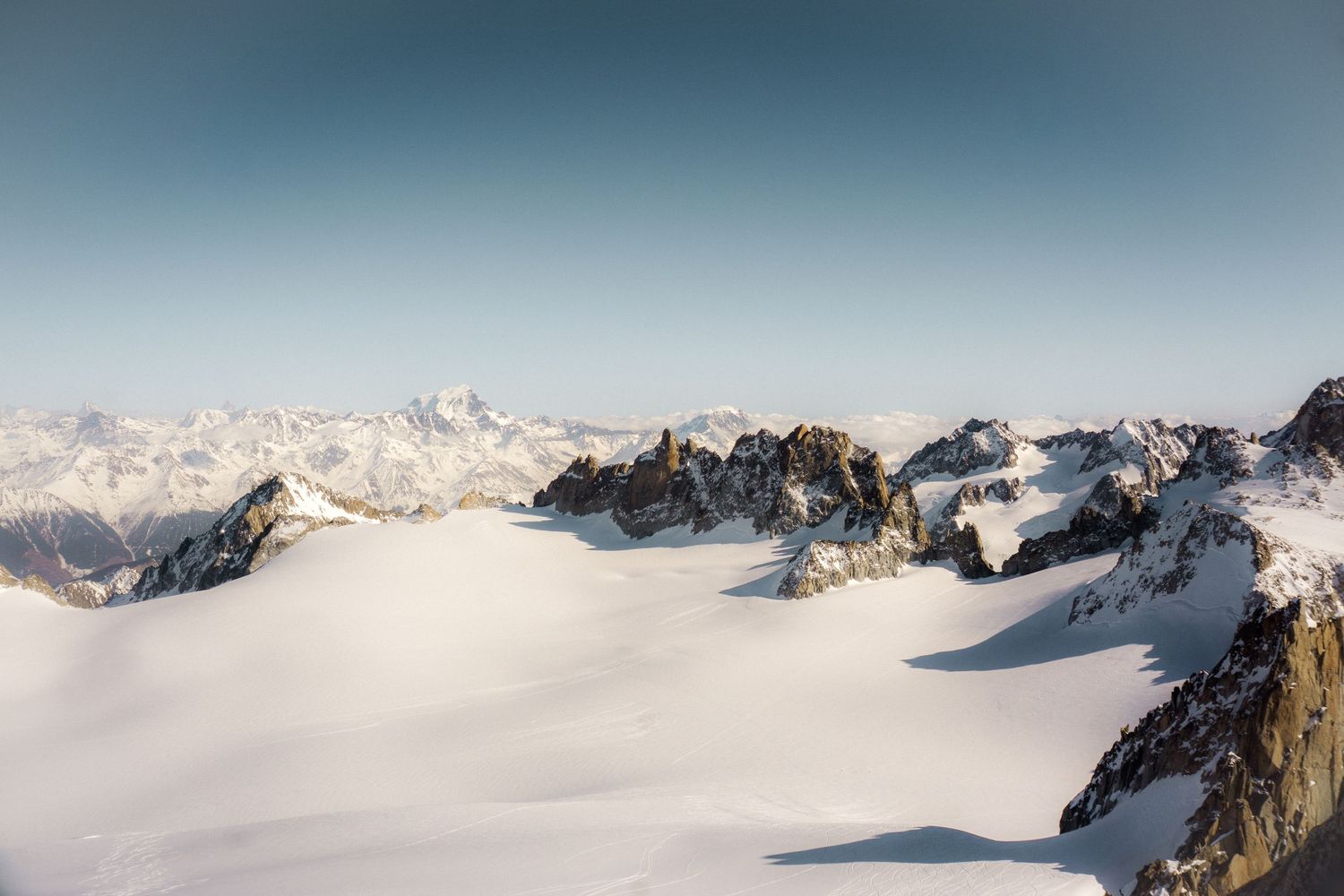 Snow-covered mountain peaks with rocky outcrops under a clear blue sky in the Alps.