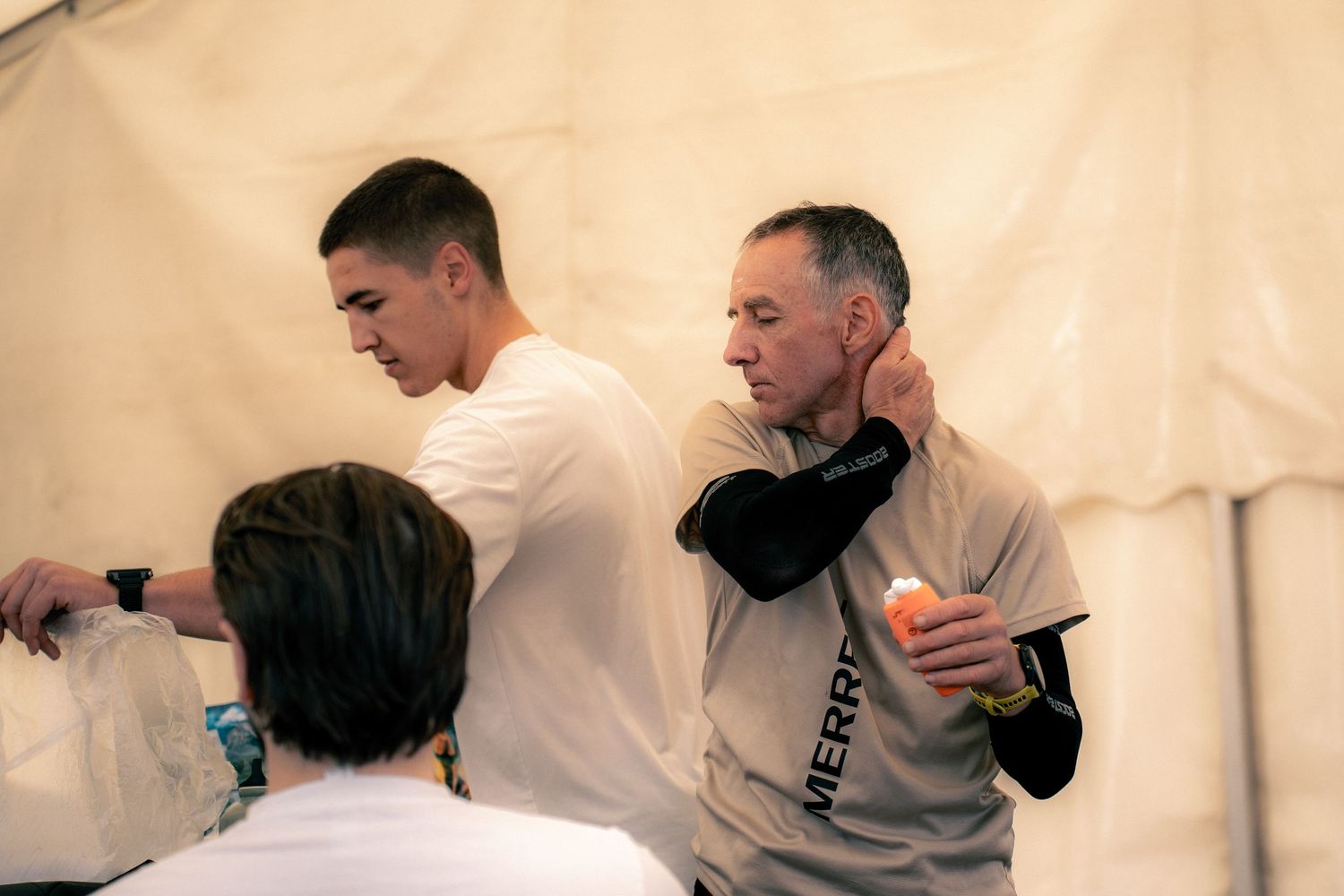 Trail runner receiving a neck massage from a support crew member inside a race medical tent.