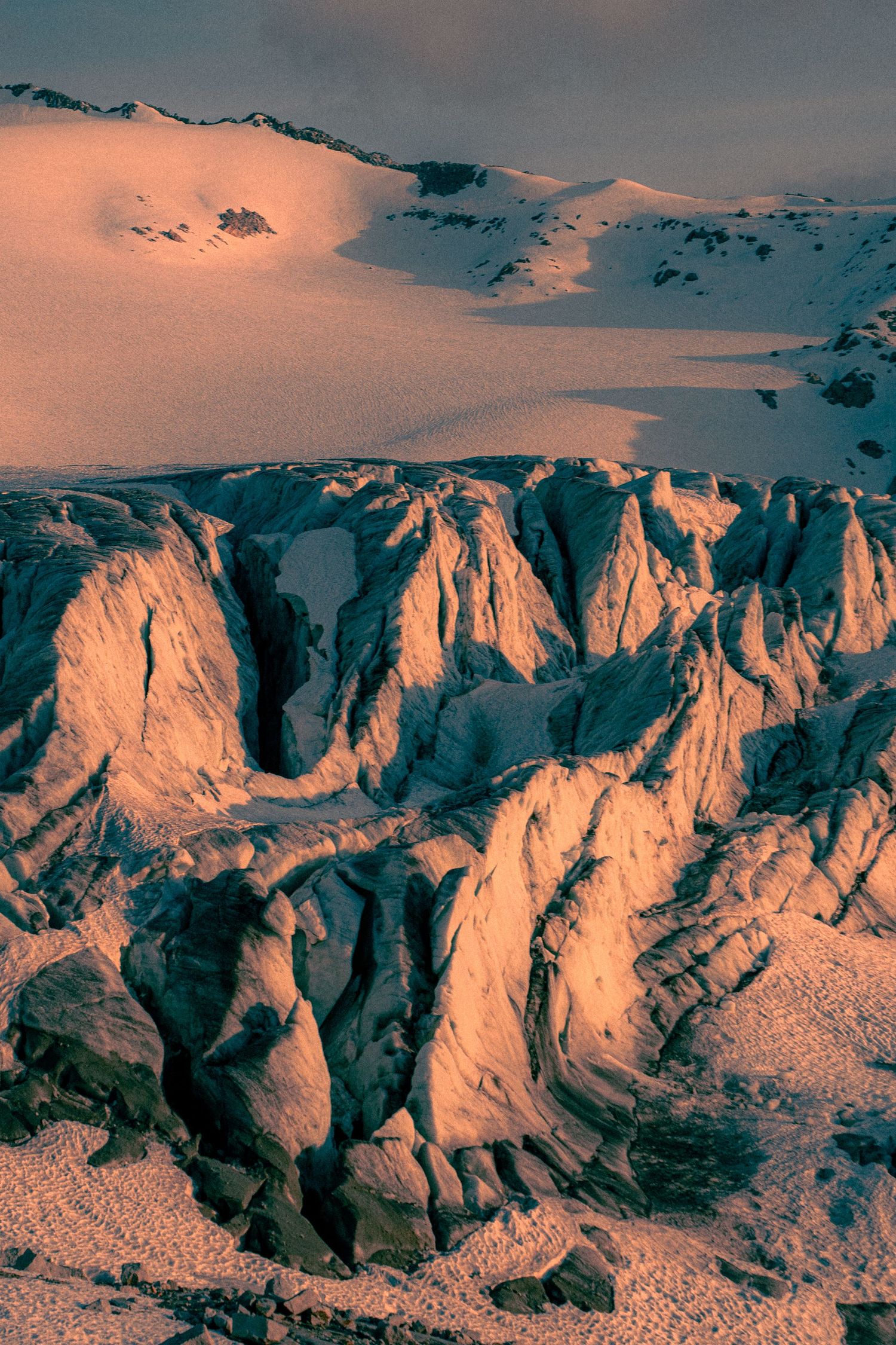 Close-up of dramatic glacier crevasses glowing in warm alpenglow light with snowy slopes above.