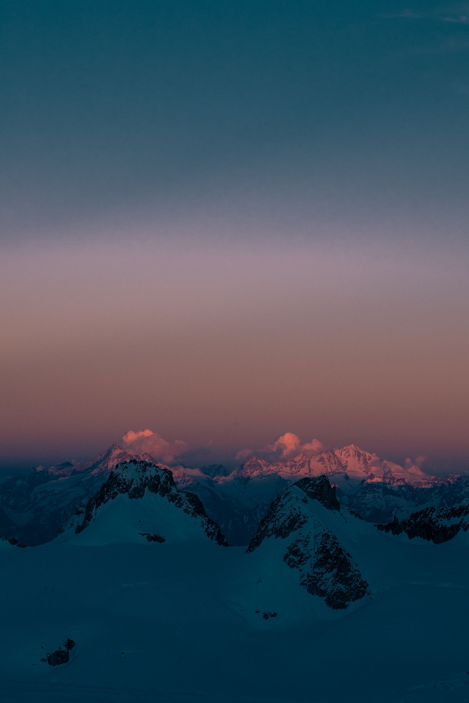 Snow-capped mountain peaks bathed in pink and purple alpenglow at sunset with a gradient teal sky above.