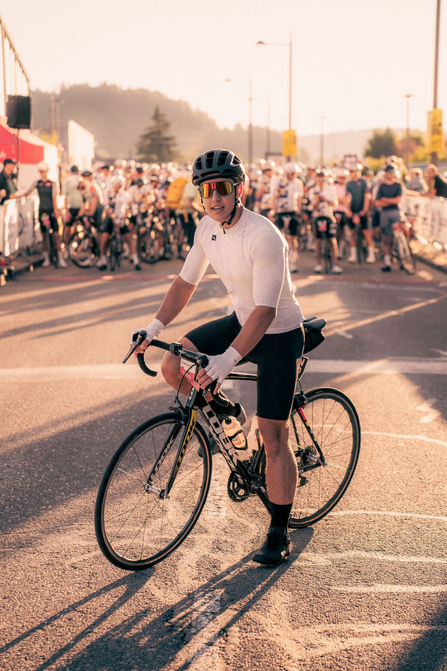 Cyclist in white jersey and helmet poses with road bike at sunny cycling event start line.