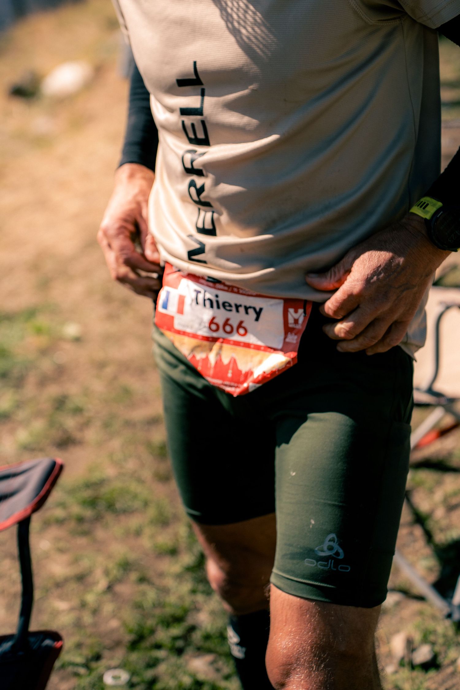 Trail runner named Thierry wearing race bib number 666 adjusting gear at race checkpoint outdoors.