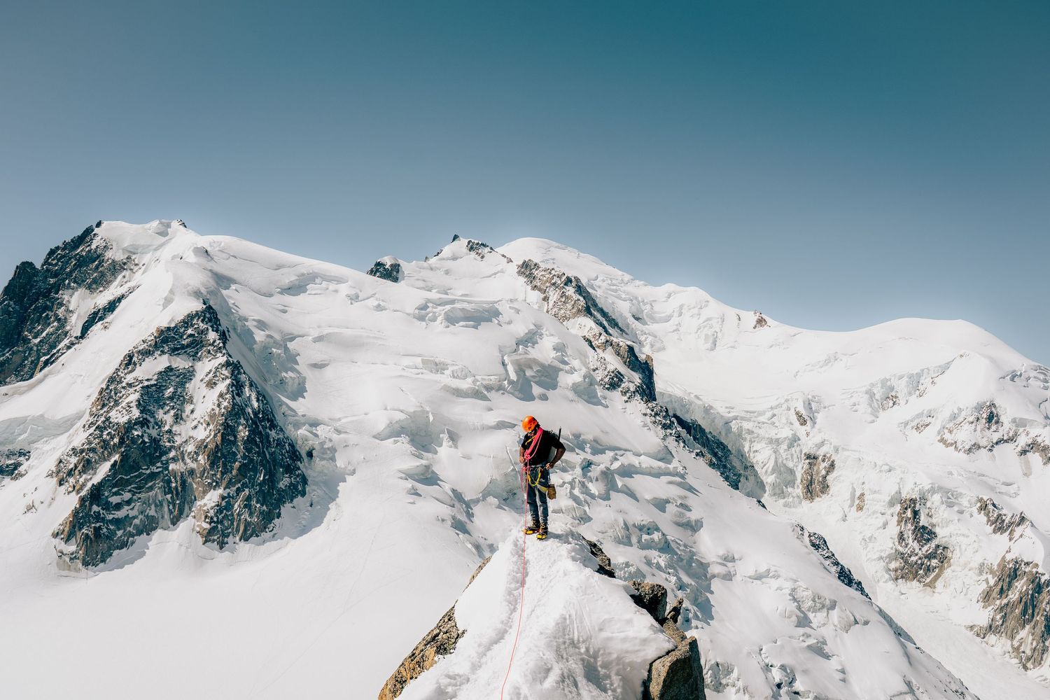 A lone mountaineer stands on a snowy ridge gazing at the majestic snow-covered peaks of Mont Blanc.