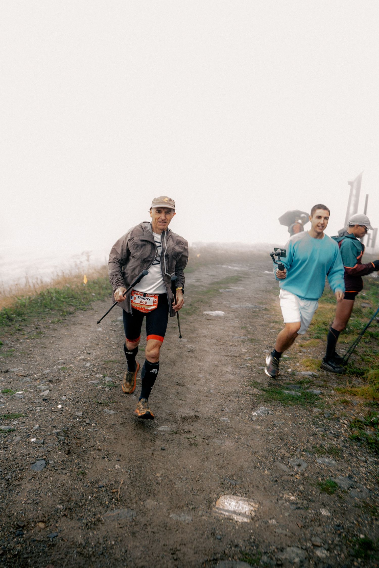 Trail runner with trekking poles and knee compression sleeves descends foggy mountain path.