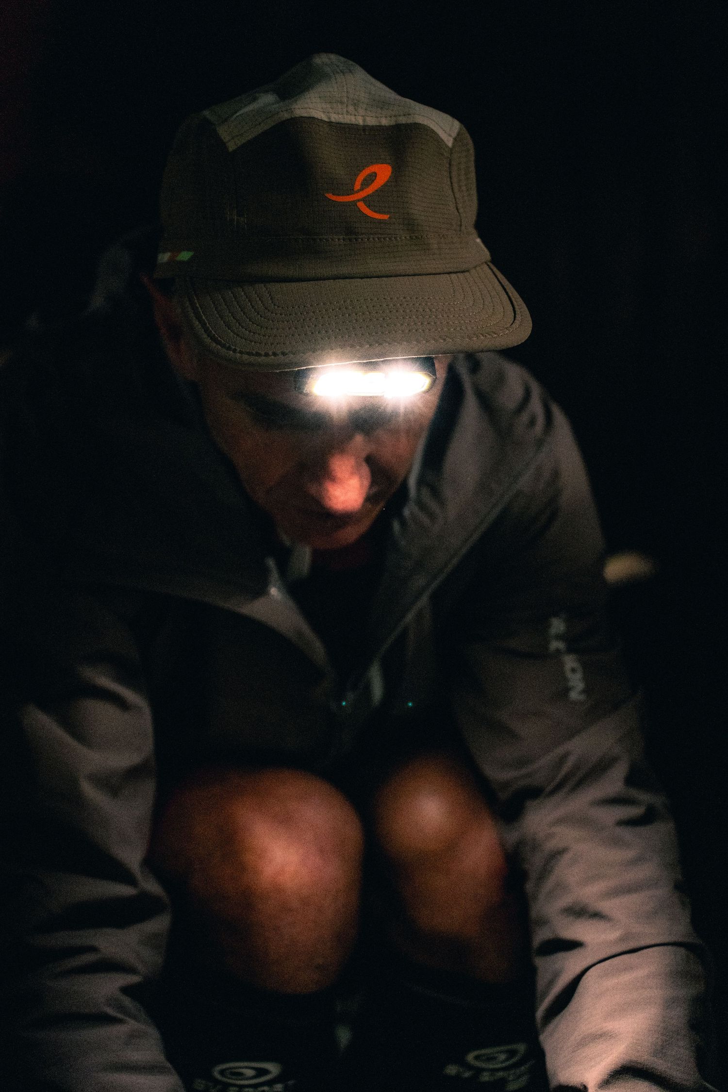 Trail runner wearing a headlamp and cap in darkness during a nighttime ultramarathon race.