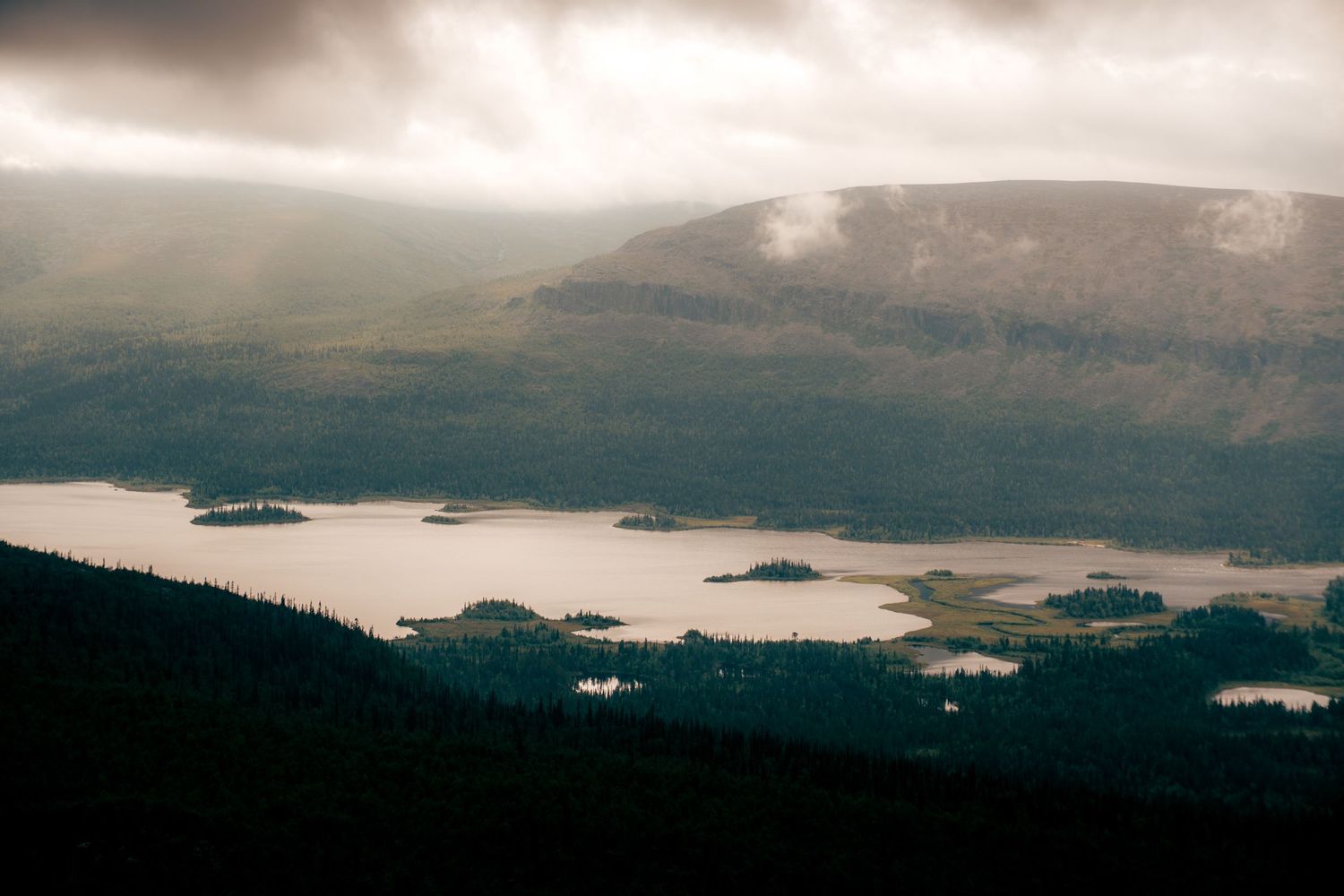 Dramatic aerial view of a mountain lake with small islands under moody storm clouds.