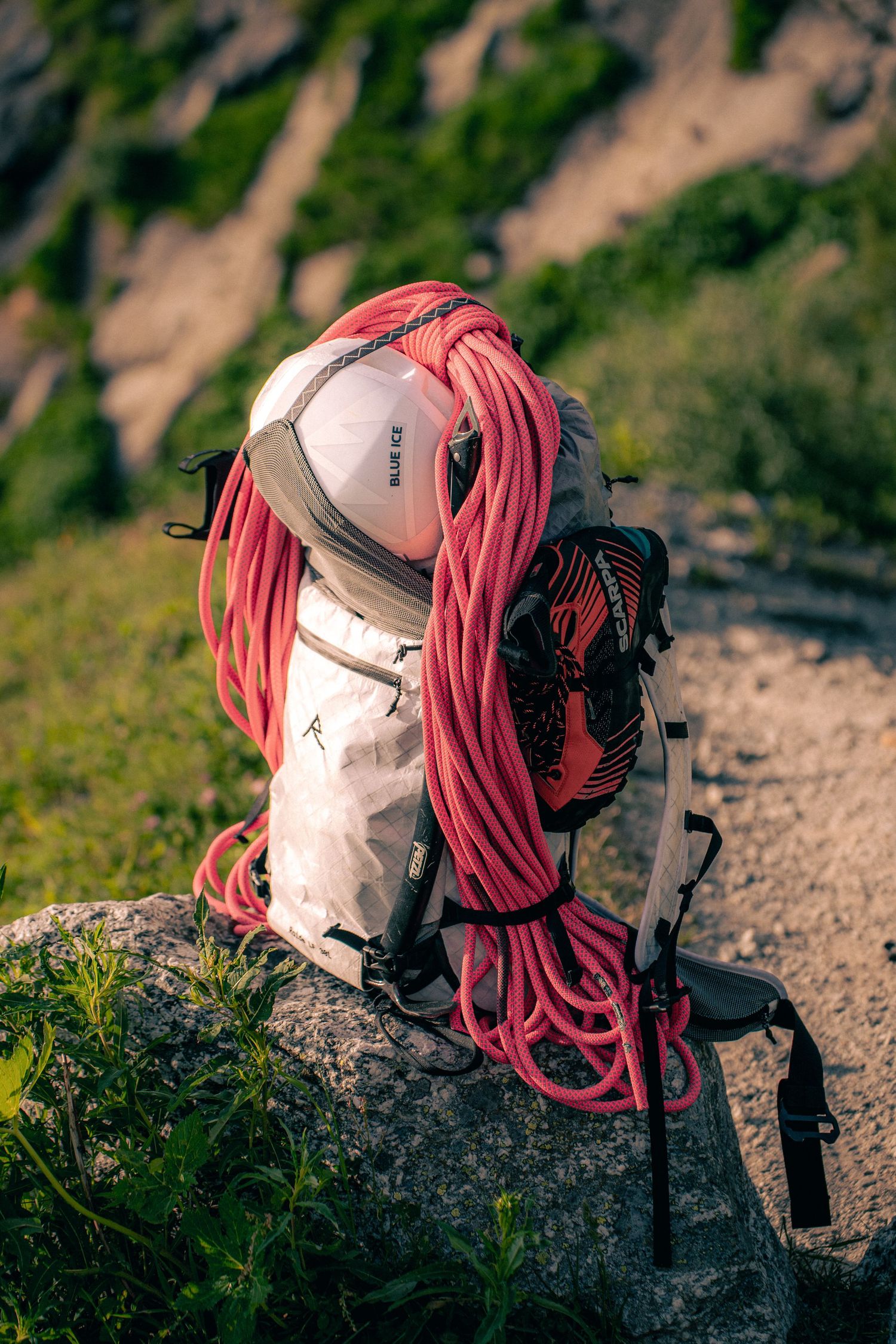 White hiking backpack with pink climbing rope and trekking pole resting on a mountain rock.