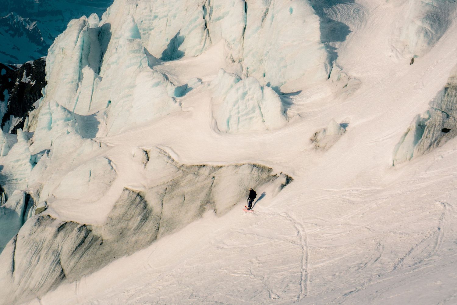 A skier descends a steep snow-covered glacier surrounded by dramatic ice formations and towering seracs.