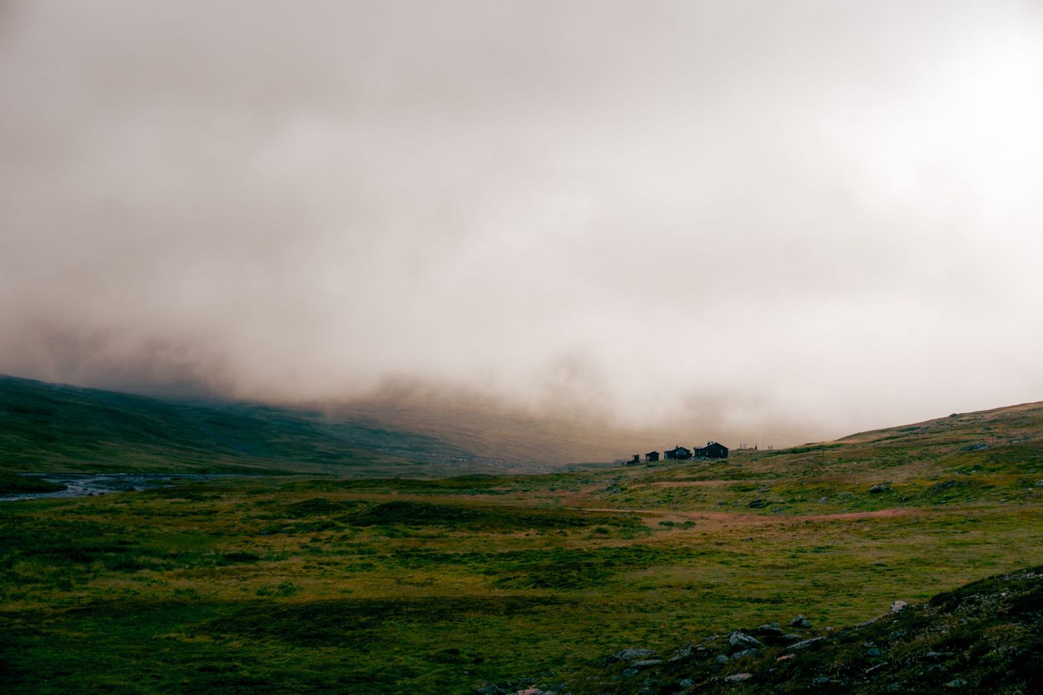 Low clouds roll over a green hillside creating a dramatic misty landscape at dusk.
