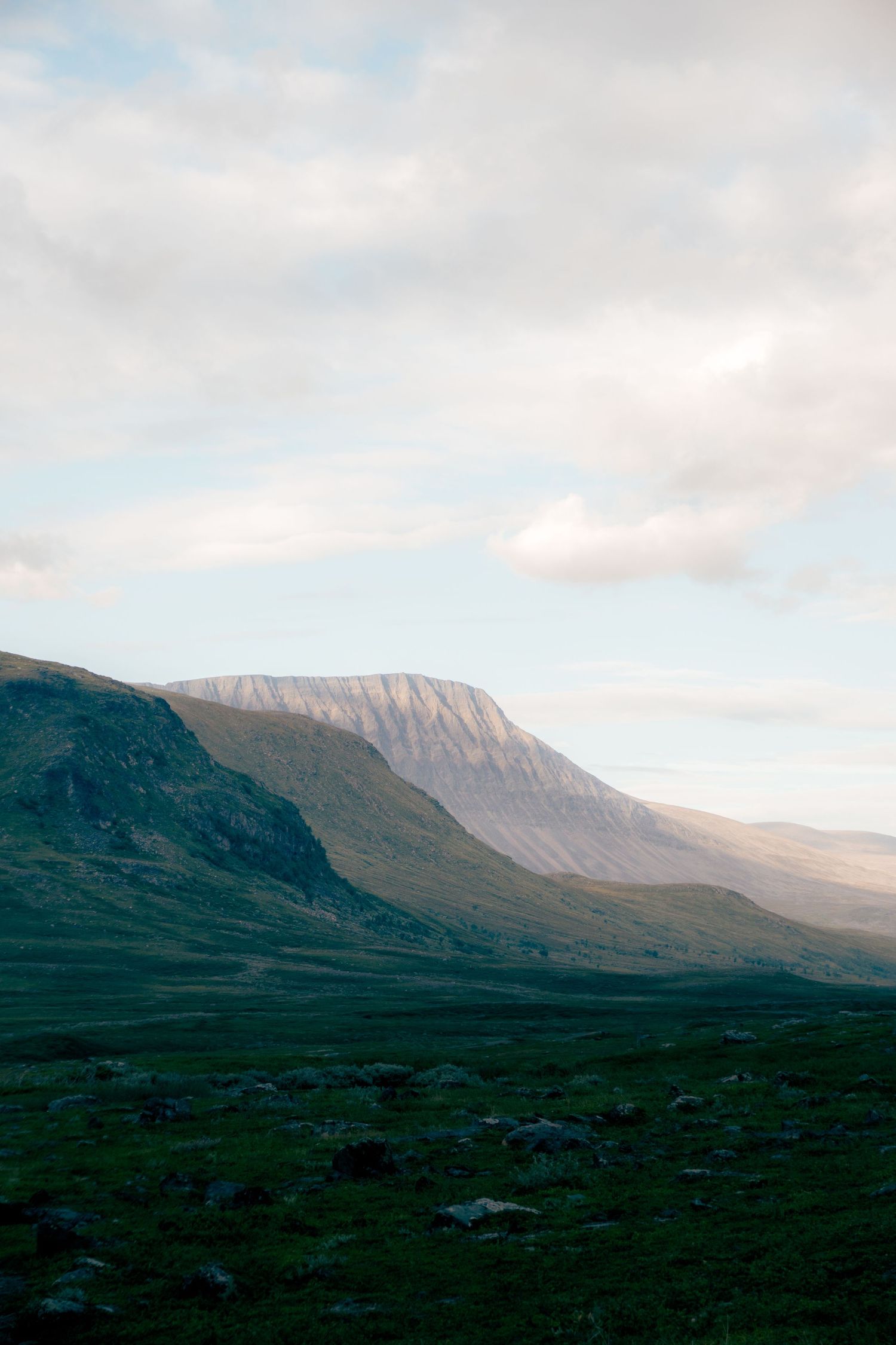Sunlit flat-topped mountain rising above a vast green highland plateau under a partly cloudy sky.