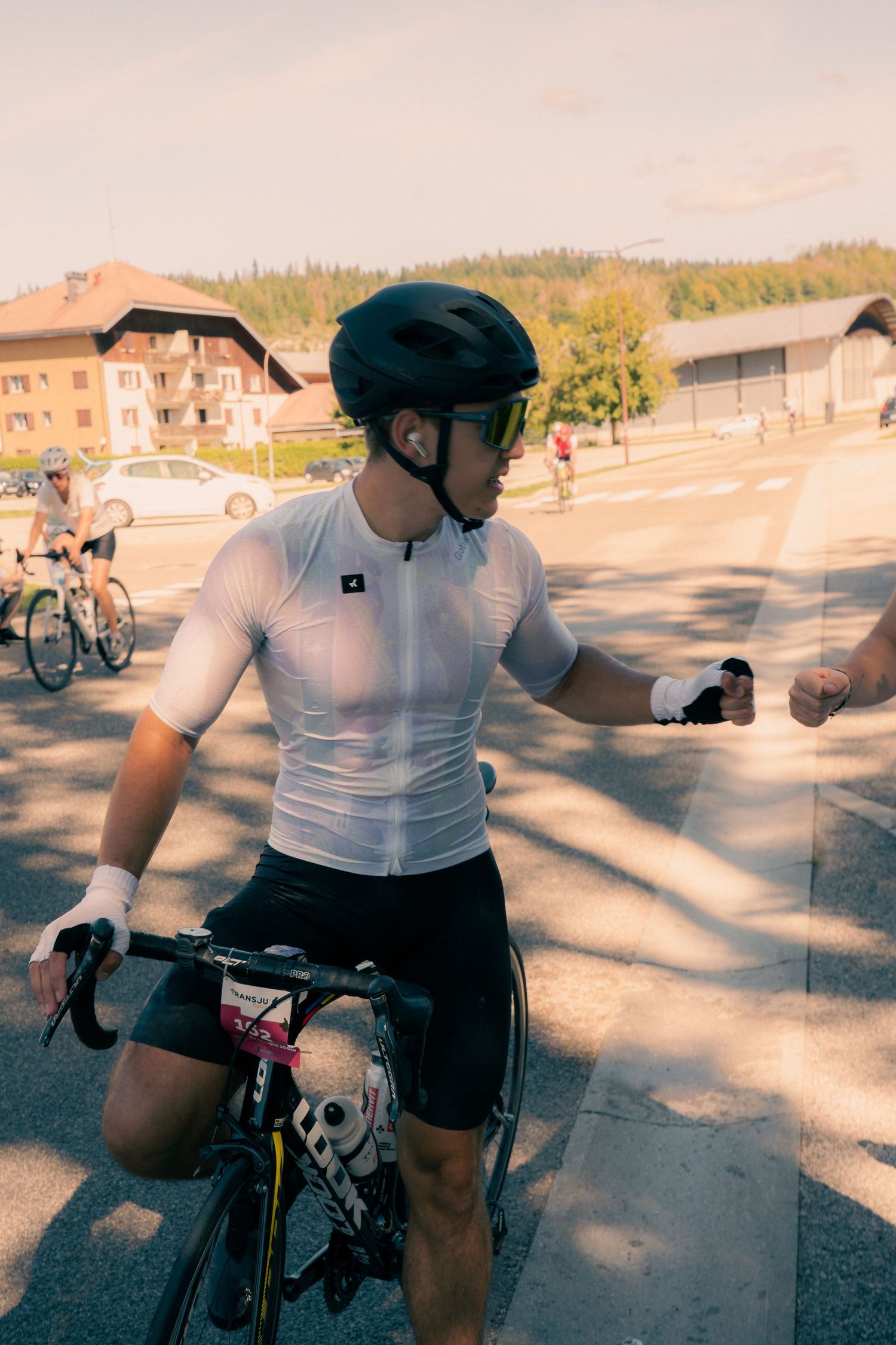 Cyclist in white jersey and black helmet fist bumping during a road cycling event in a European town.