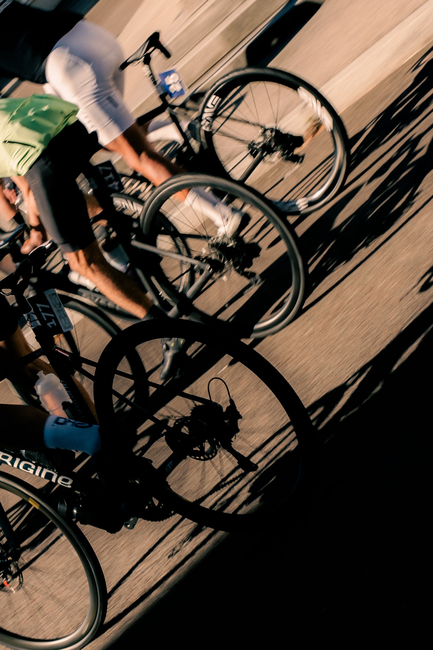 Two cyclists riding bikes cast dramatic shadows on a sunlit street, captured with motion blur effect.