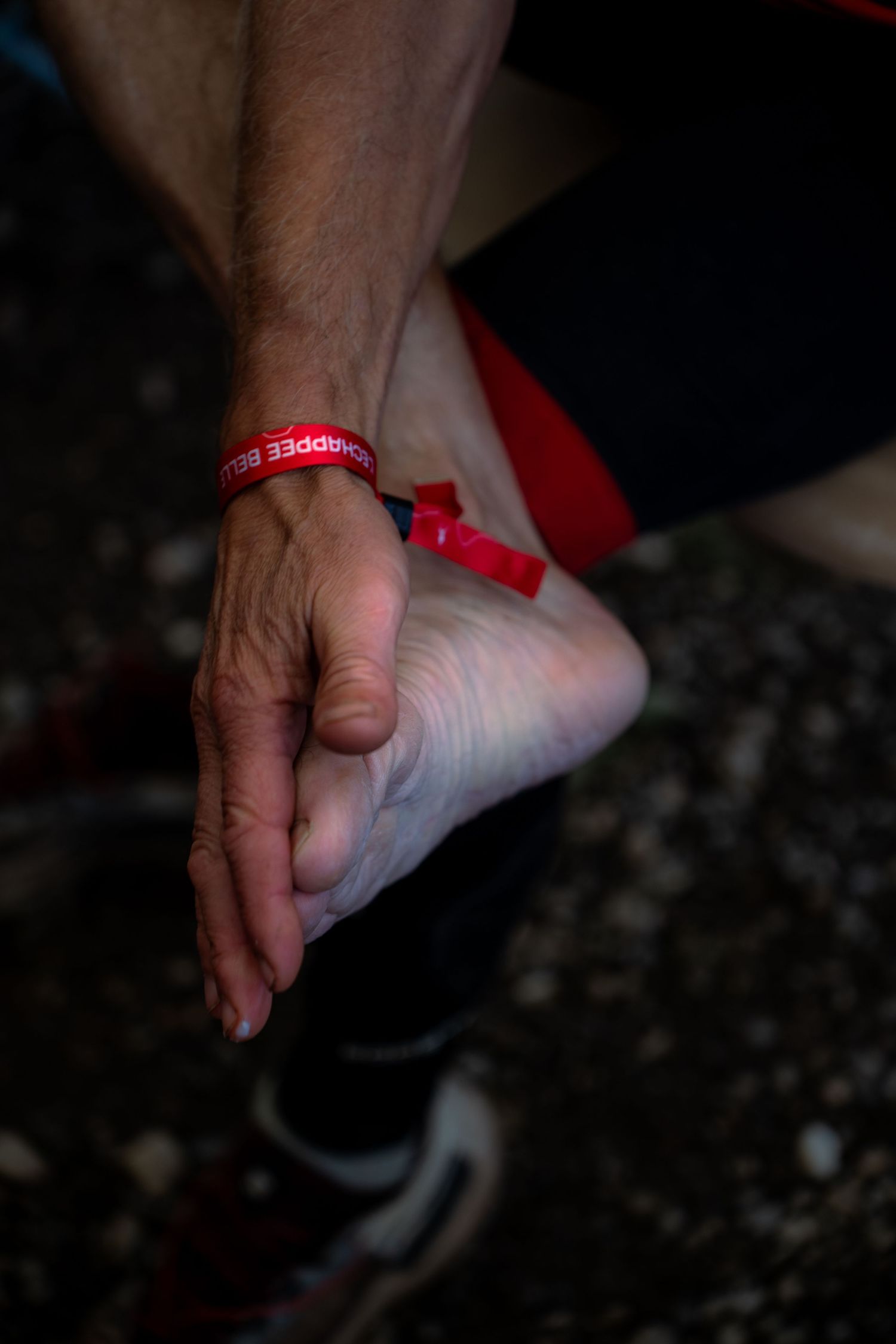 Close-up of an athlete's hand massaging their foot wearing a red charity wristband during a race.