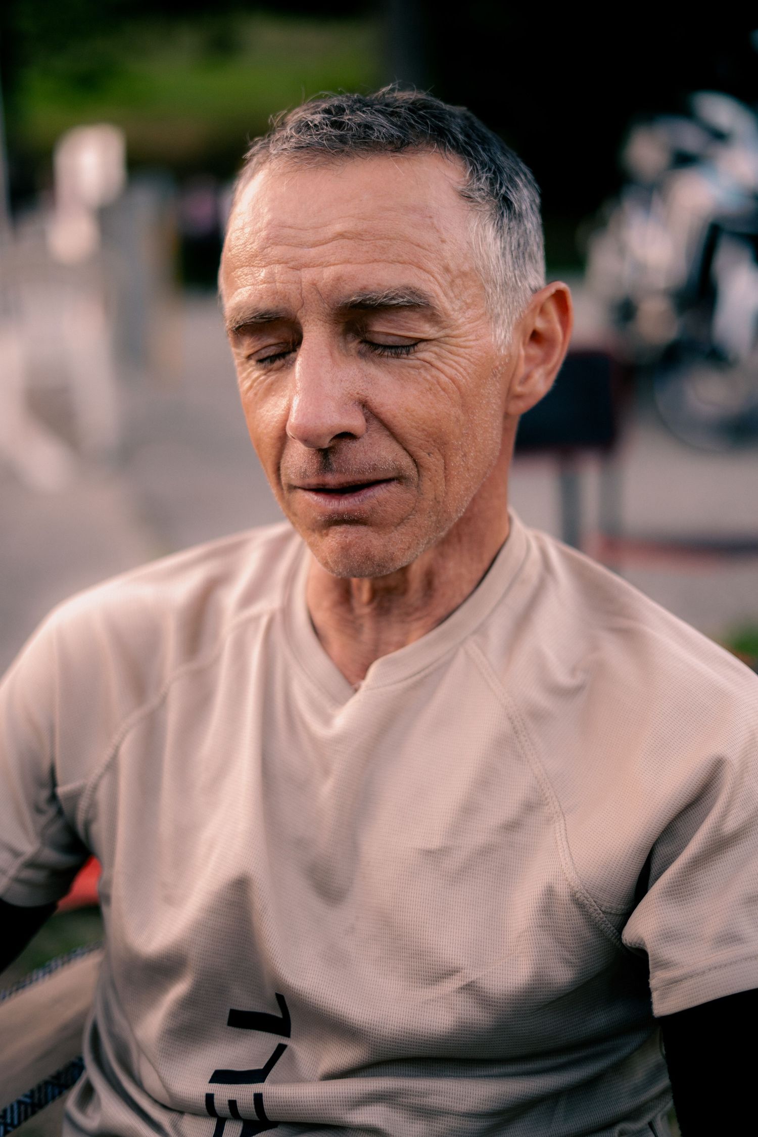 Close-up portrait of a fit older man with gray hair wearing a beige athletic shirt outdoors.