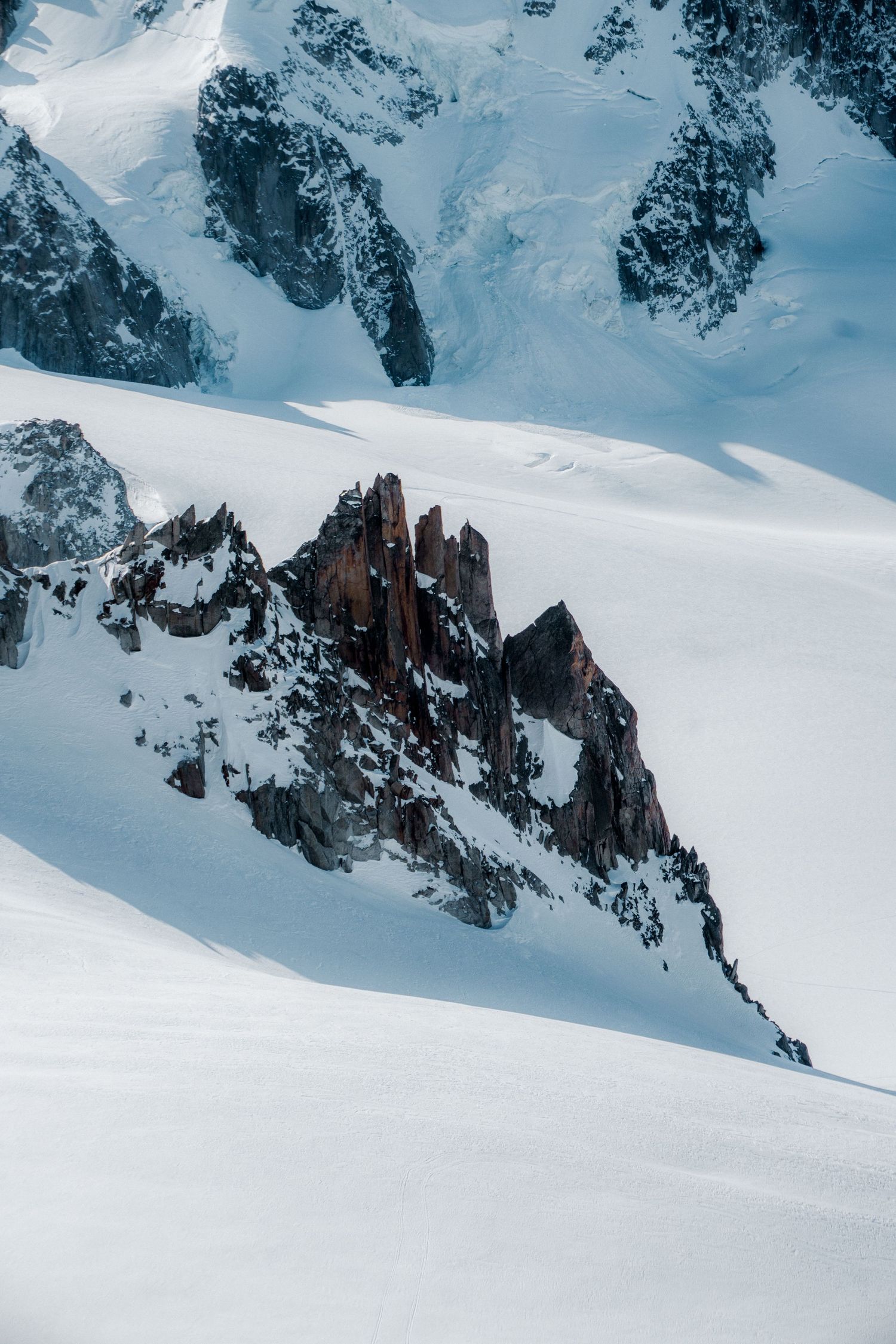 Snow-covered alpine mountain landscape with dramatic dark rocky spires emerging from a vast white glacier in the Alps.