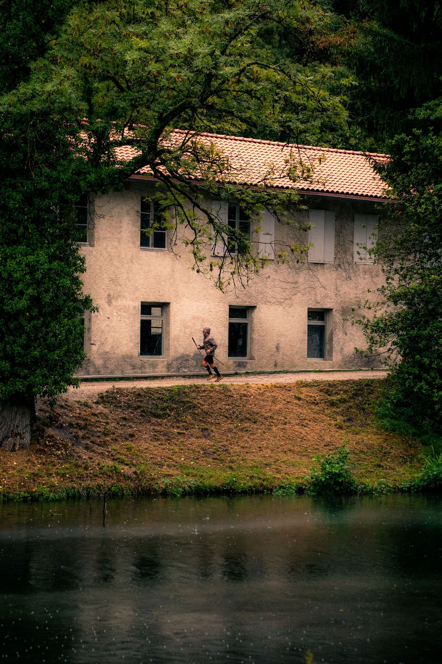 Solo trail runner passes old stone building beside calm reflective lake.