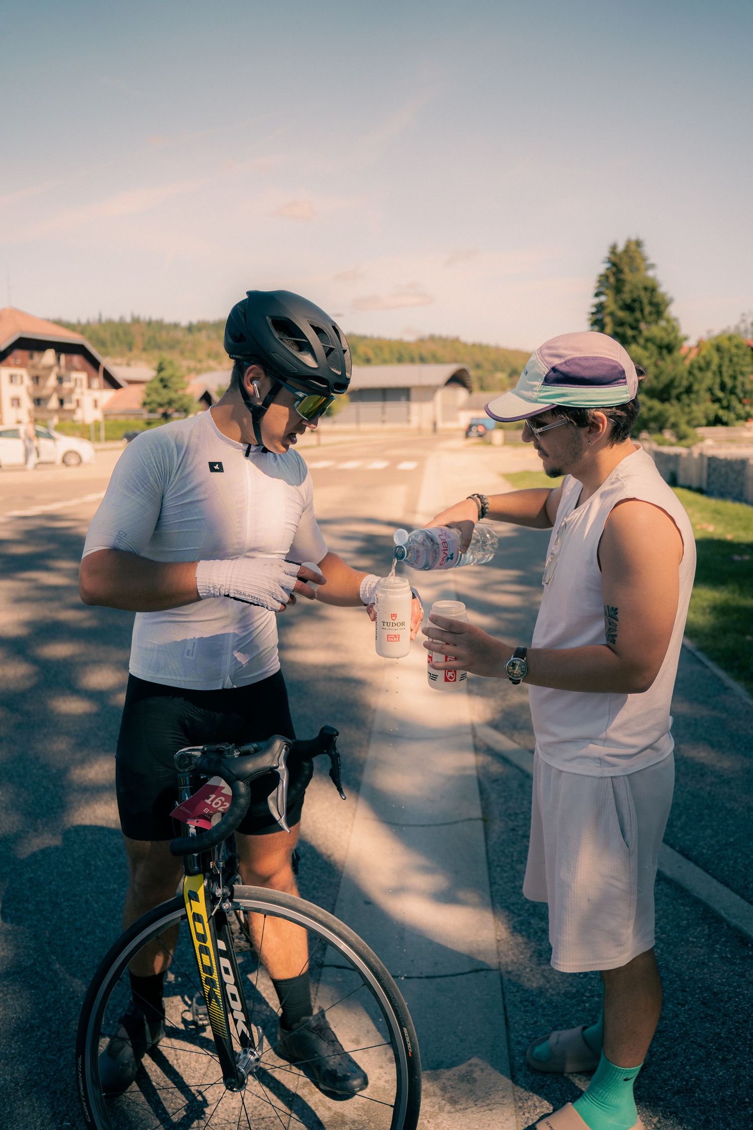 Cyclist in helmet receives water bottle from supporter during outdoor road cycling break on sunny day.