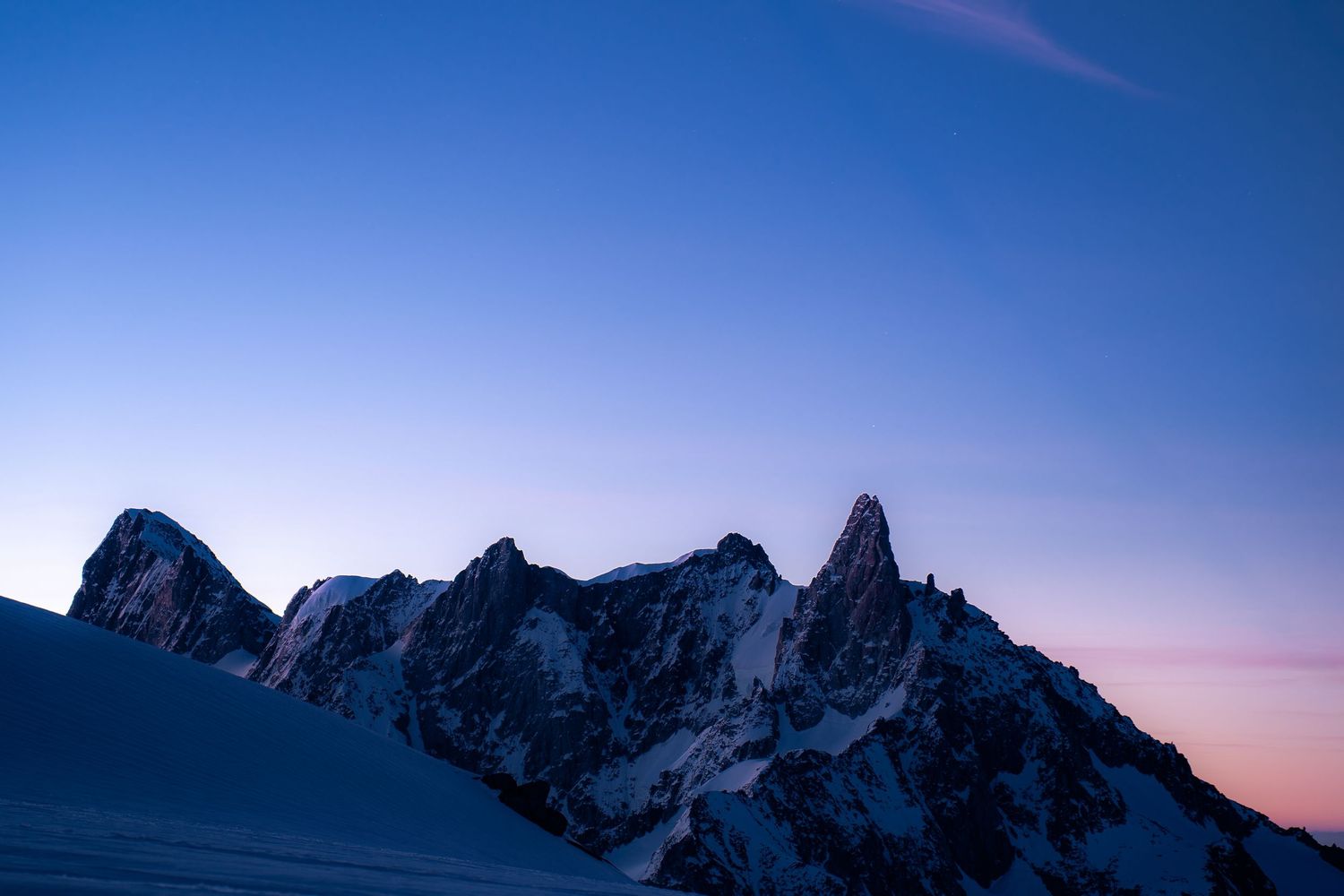 Jagged snow-dusted mountain peaks silhouetted against a blue and pink twilight sky at dusk.