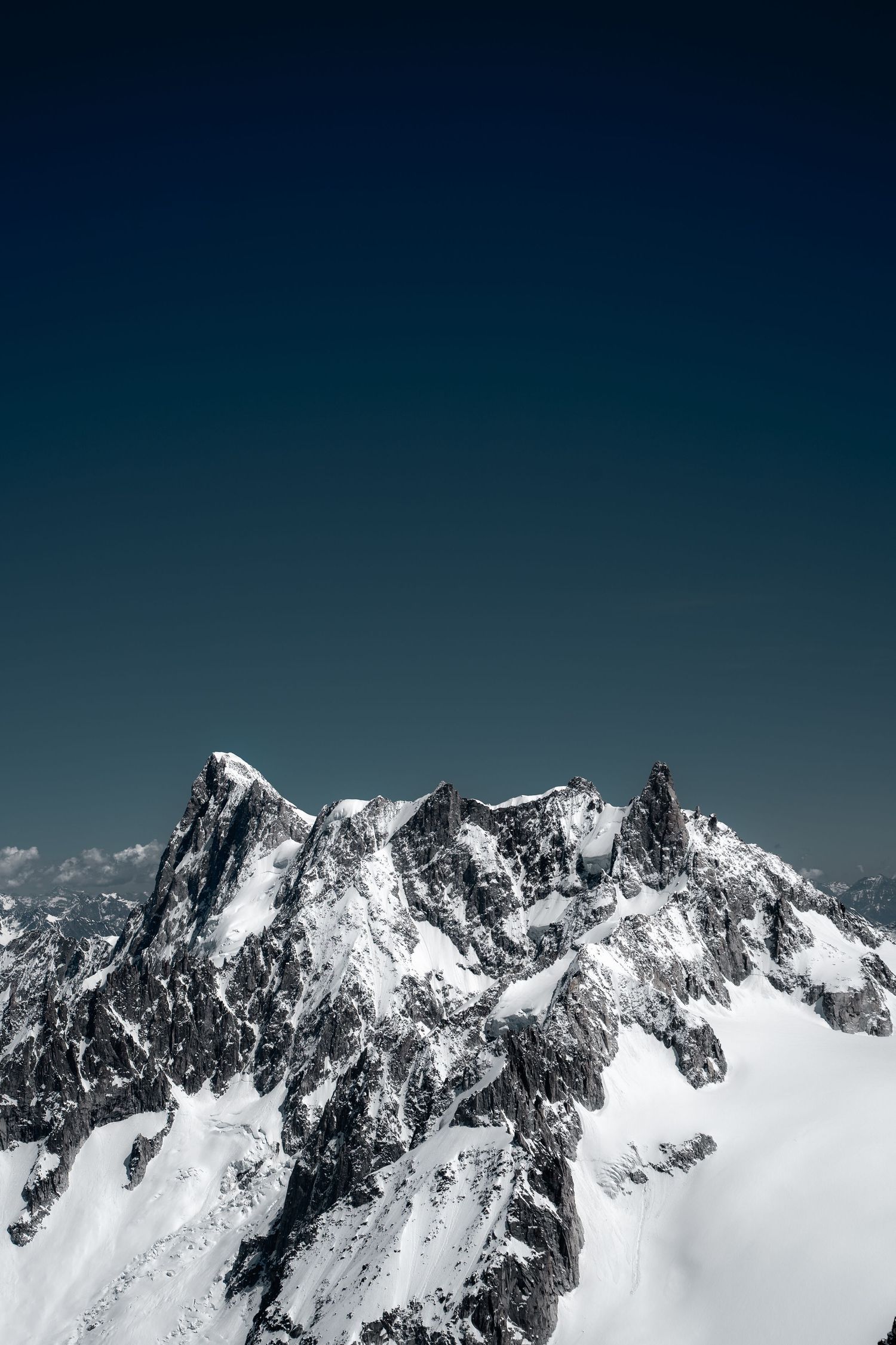 Dramatic snow-covered jagged mountain peaks rising against deep blue sky in pristine alpine wilderness.