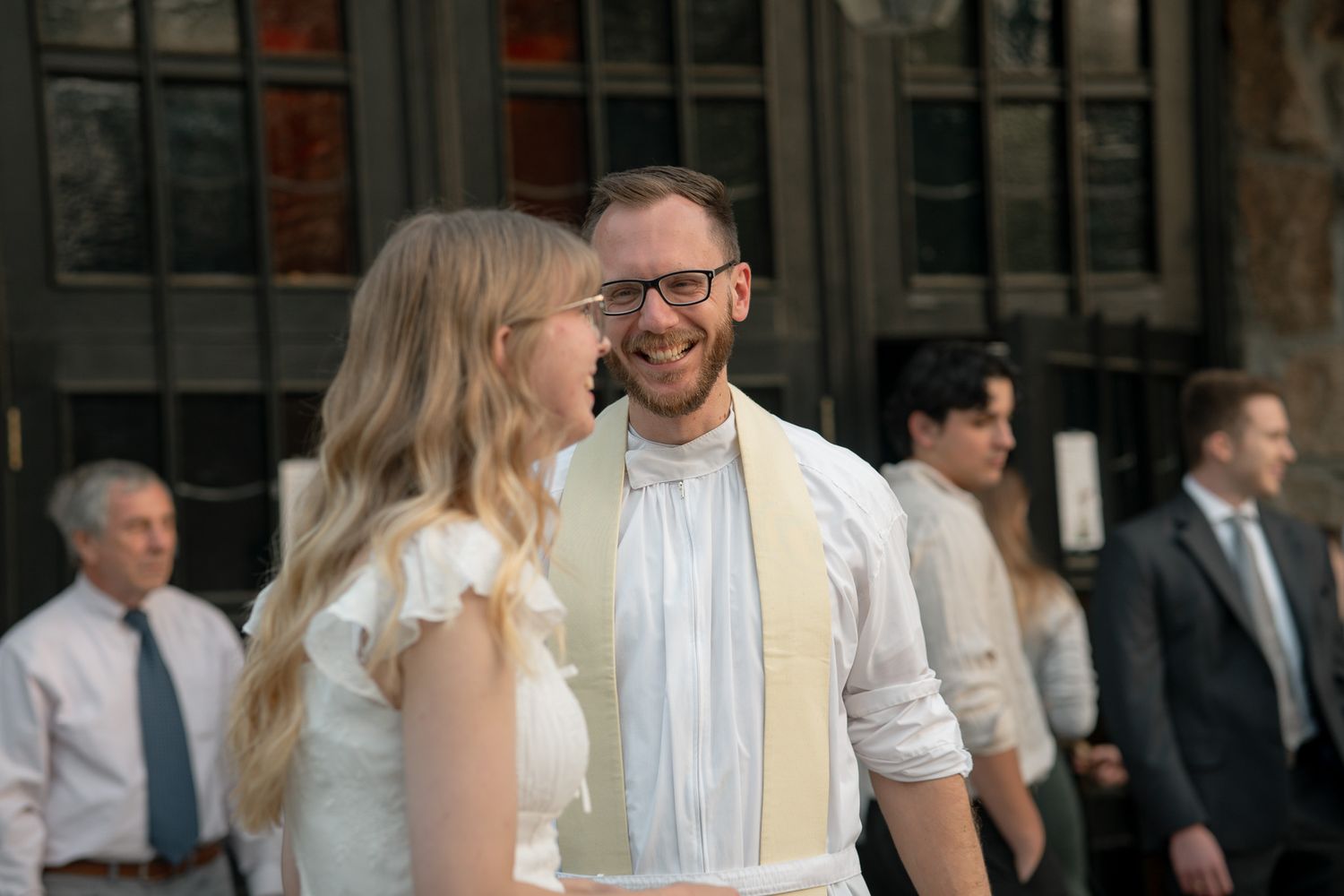 A smiling catholic priest in glasses stands with a student in a white dress before Easter Vigil outside UGA's Catholic Center.