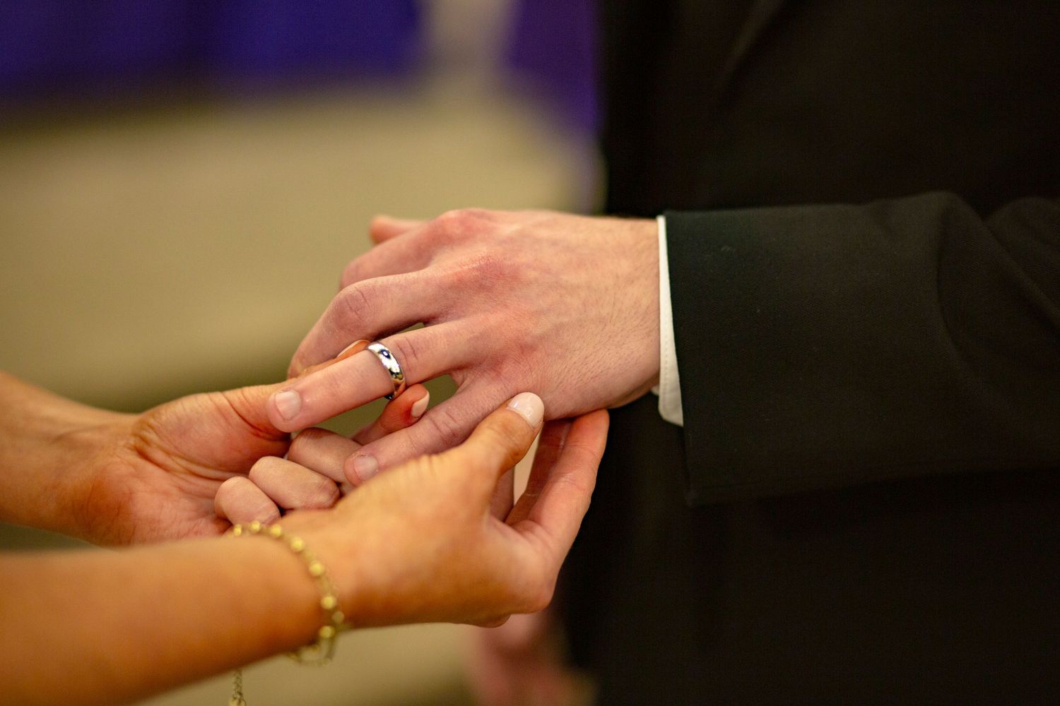 Bride placing a wedding ring on groom's finger during a catholic wedding mass, close-up of hands.