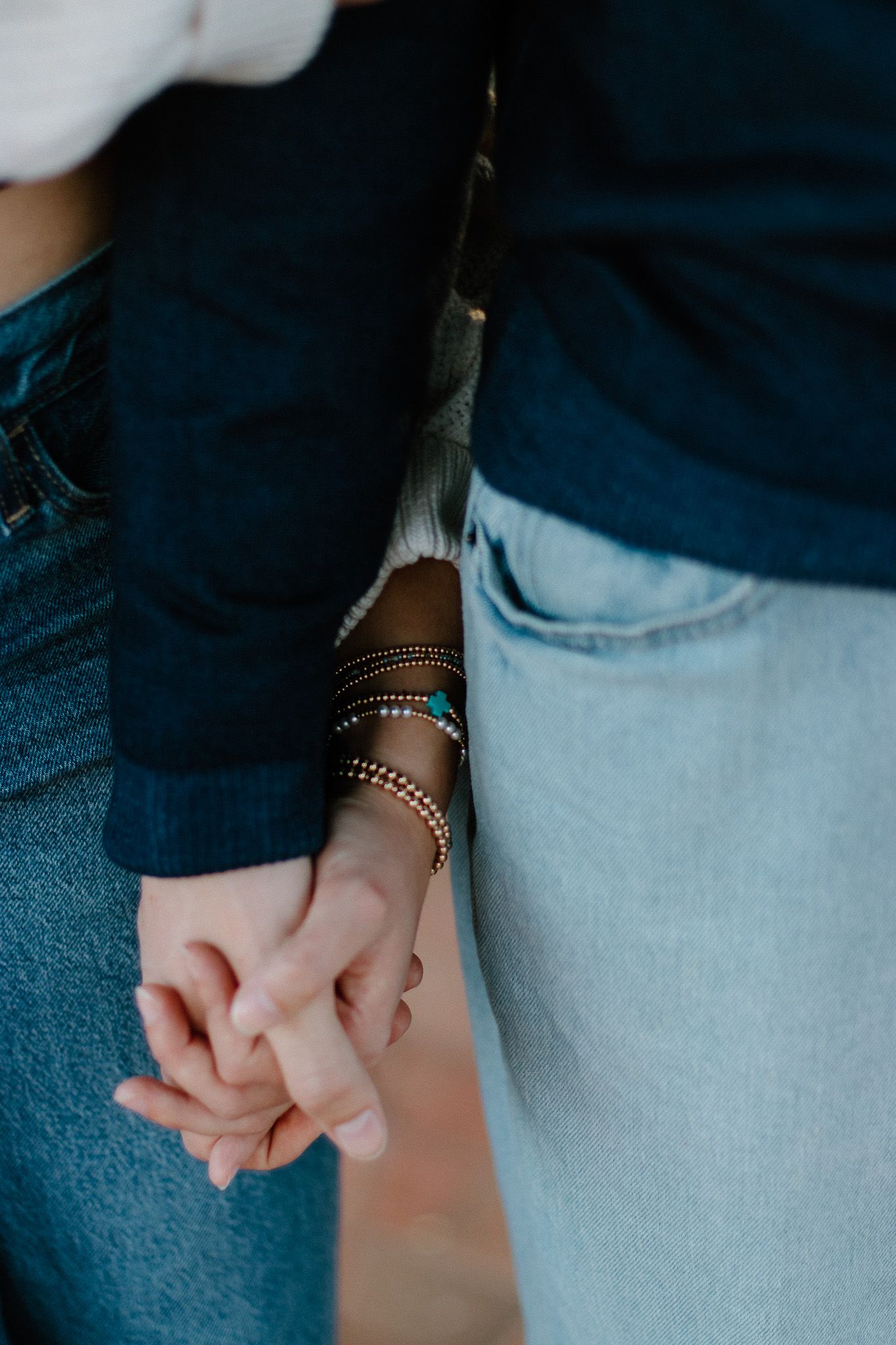 Close-up of Catholic couple holding hands with layered beaded bracelets on wrist in Athens, GA for engagement photos.