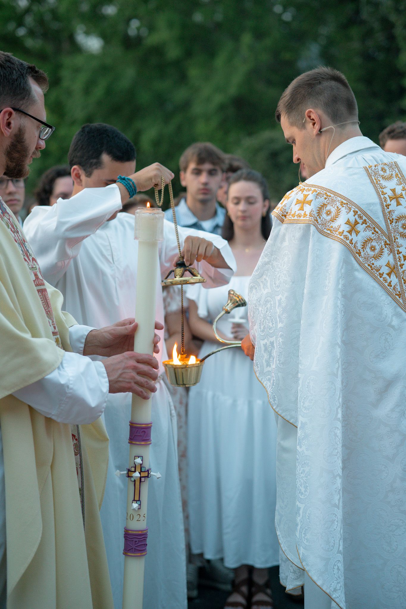 Catholic priests lighting a Paschal candle during an outdoor Easter Vigil ceremony with altar servers in white robes in Athens, GA.