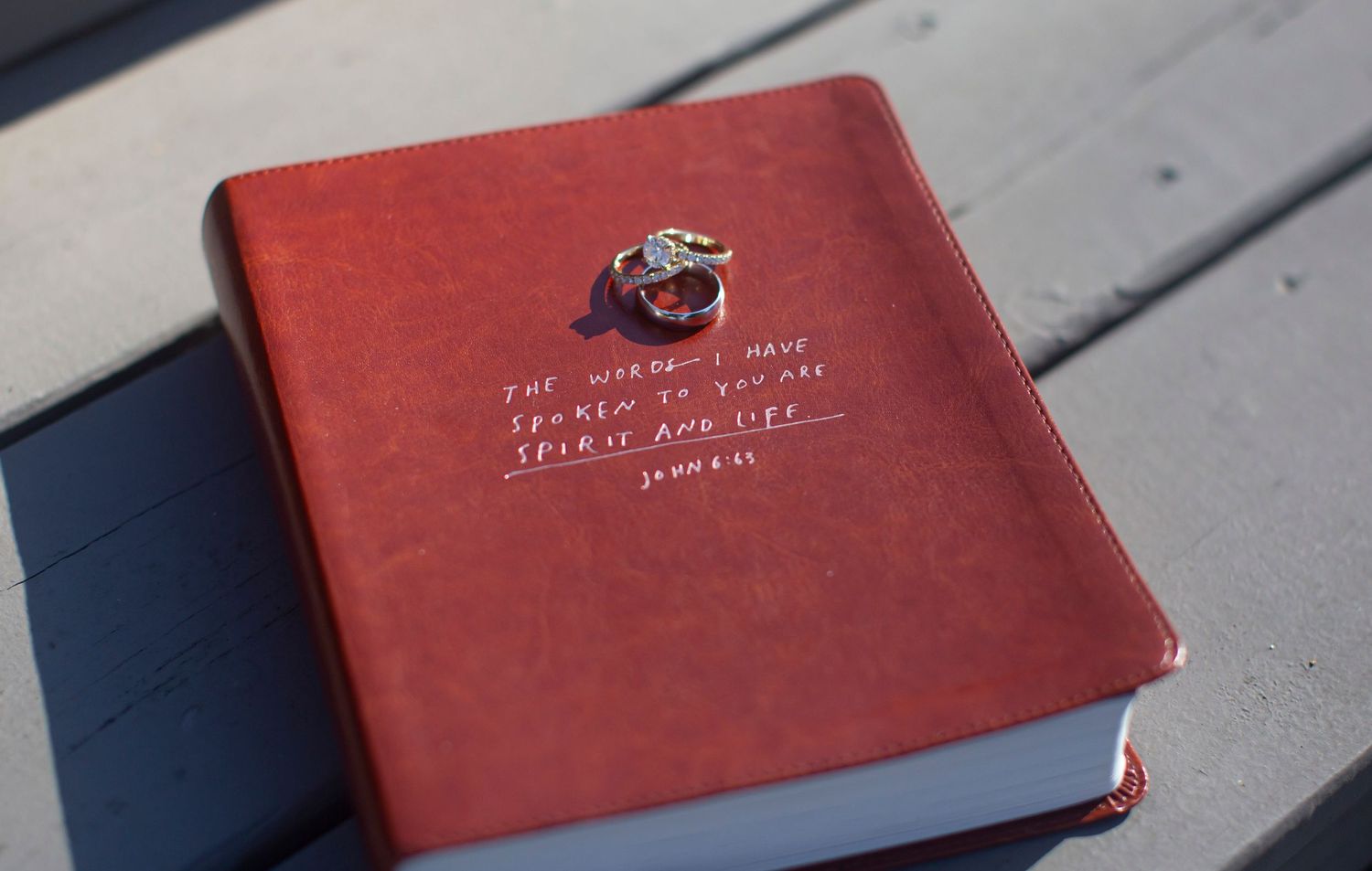 Red leather Bible with John 6:63 scripture quote and wedding rings on wooden surface before catholic wedding.