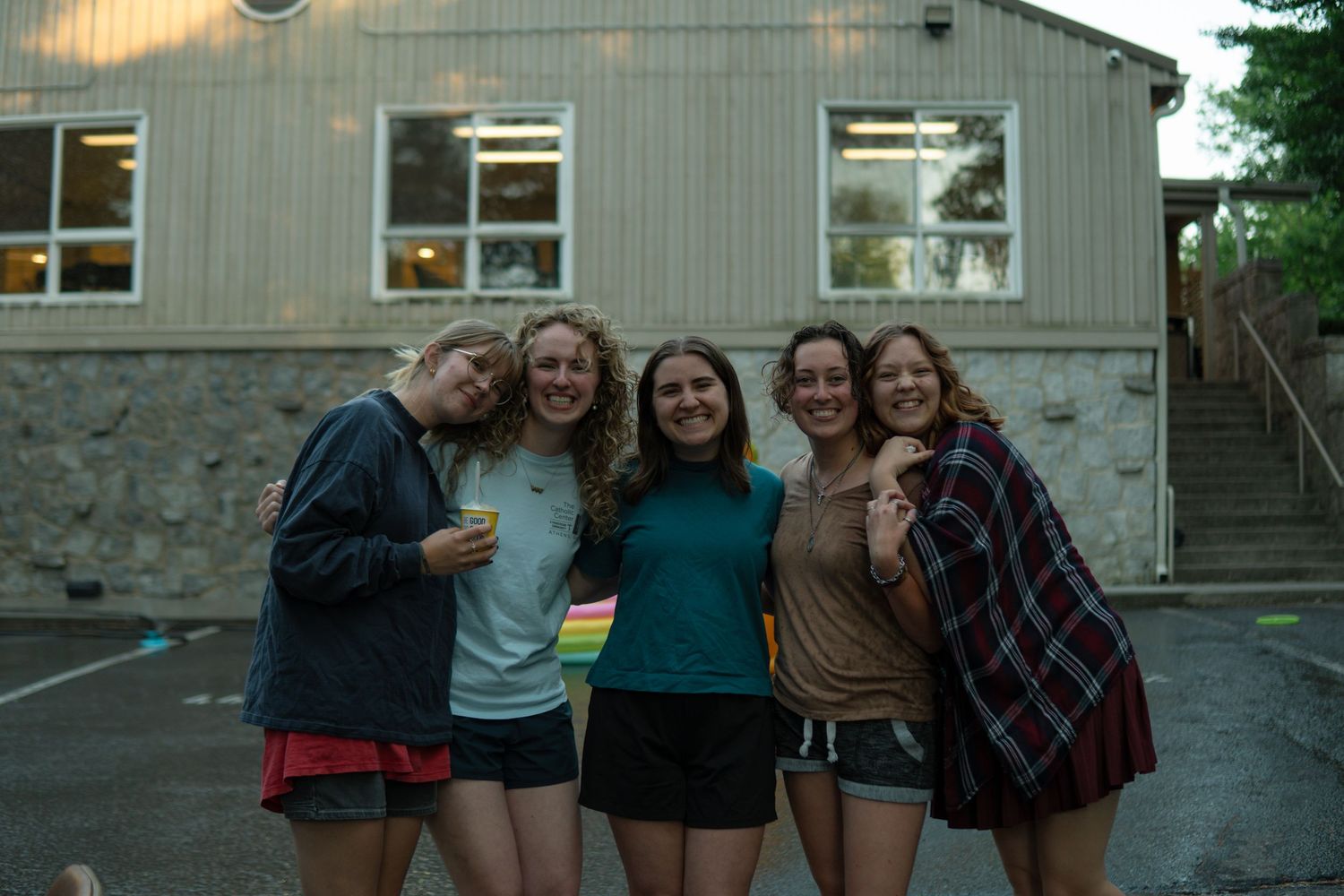 Five young women smiling together outdoors in the evening near a building at a Catholic event in Athens, GA.