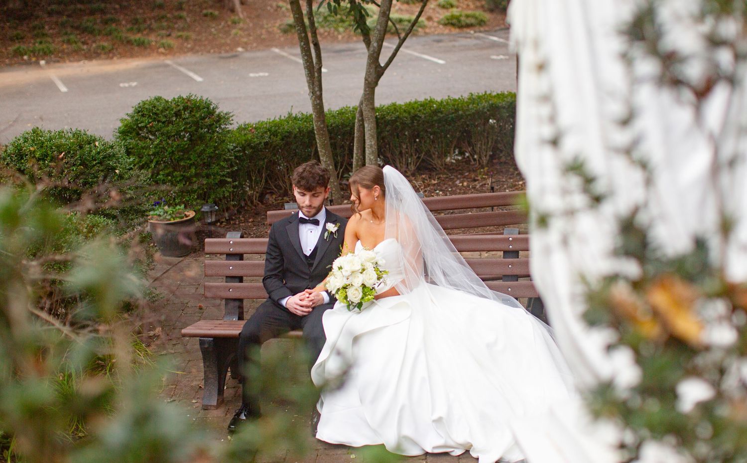 Bride and groom sitting on a wooden bench in a lush garden, sharing an intimate moment on their Catholic wedding in Athens, GA.