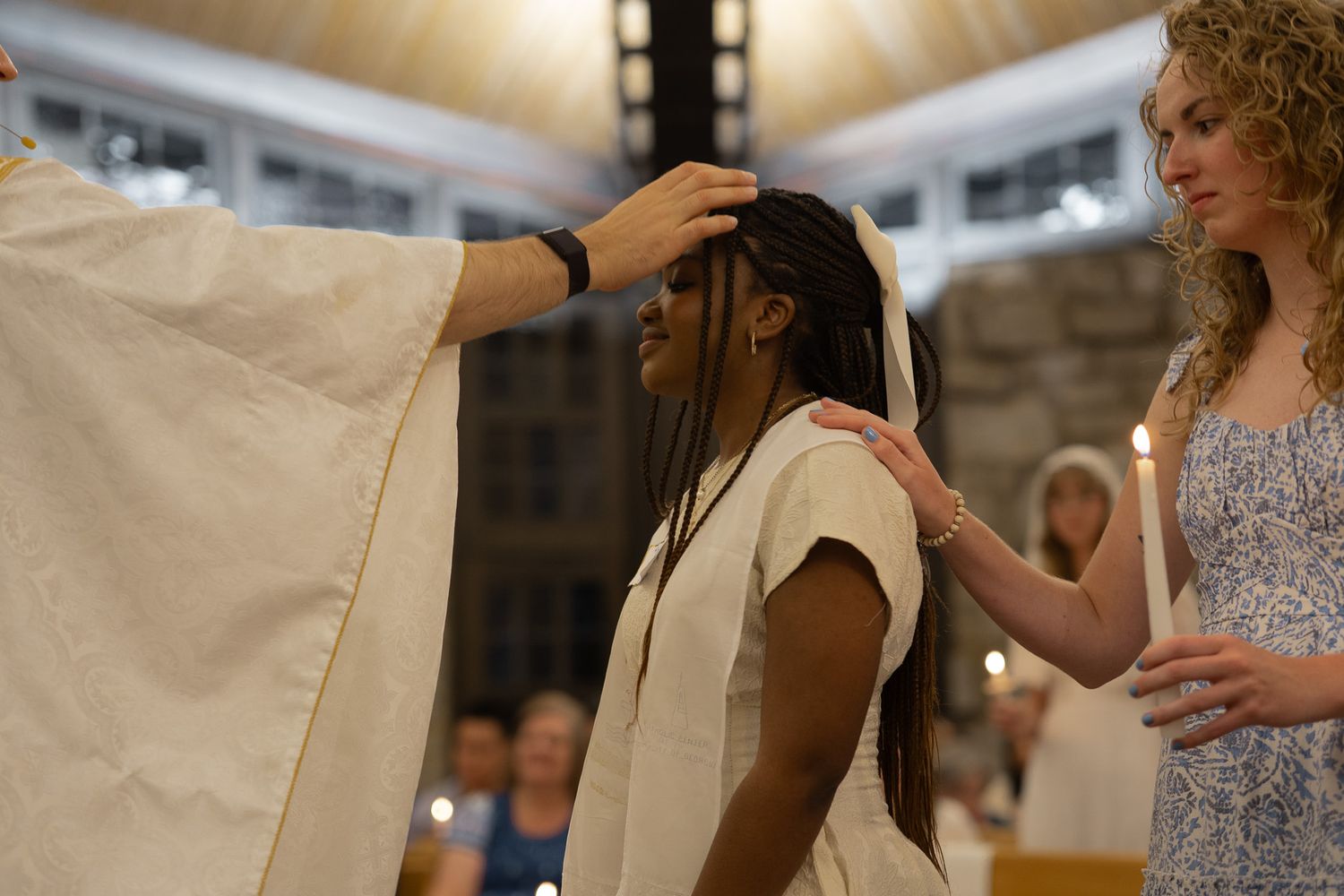 Young woman receiving sacramental blessing with hands on head during Catholic confirmation ceremony with candle in Athens, GA.