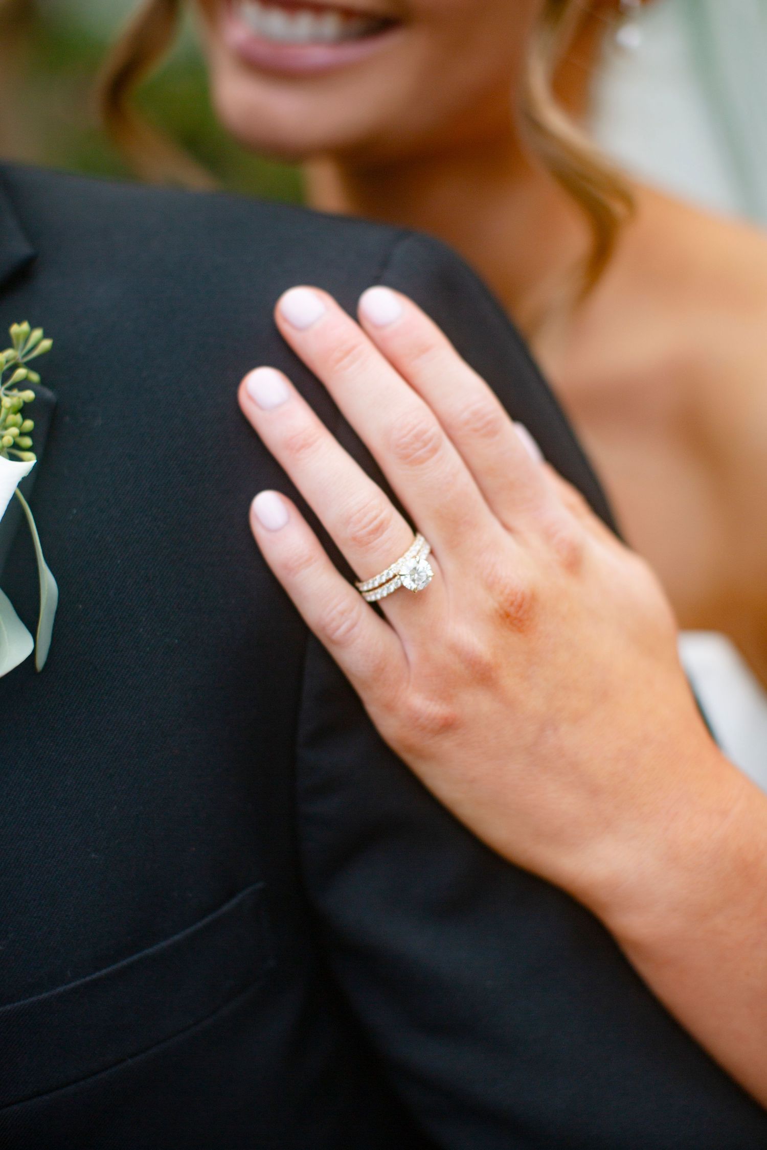 Close-up of bride's hand with diamond wedding ring set resting on groom's black tuxedo jacket outside catholic church in Athens, GA.