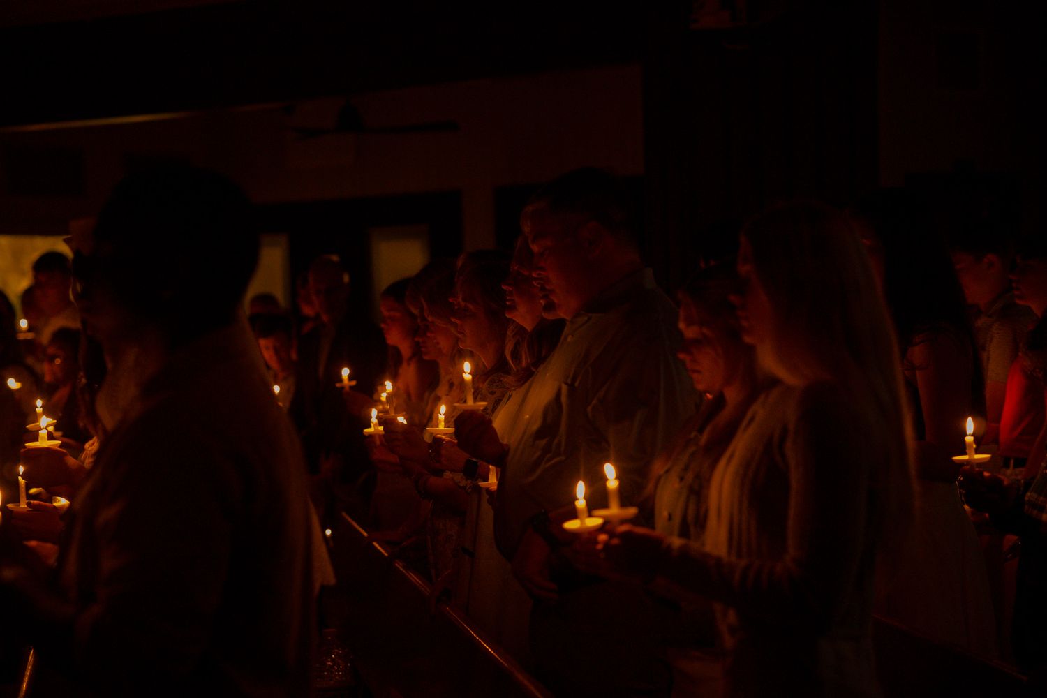 Group of people holding candles in a dark candlelight Catholic vigil.