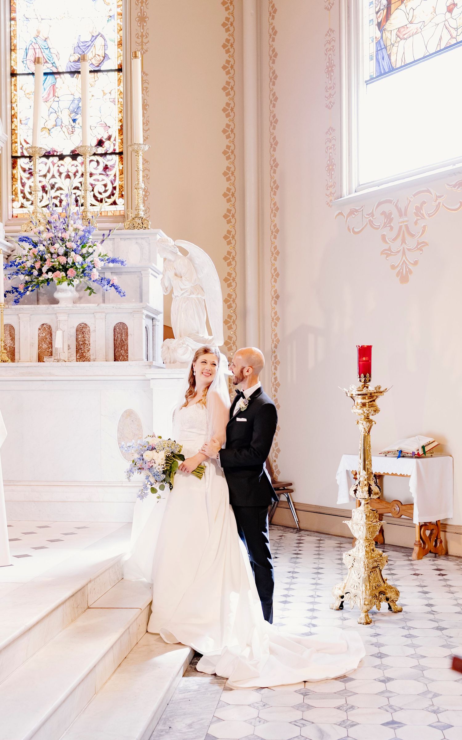 Bride and groom share a romantic moment at a white catholic church altar with stained glass windows and floral arrangements in Augusta, GA.