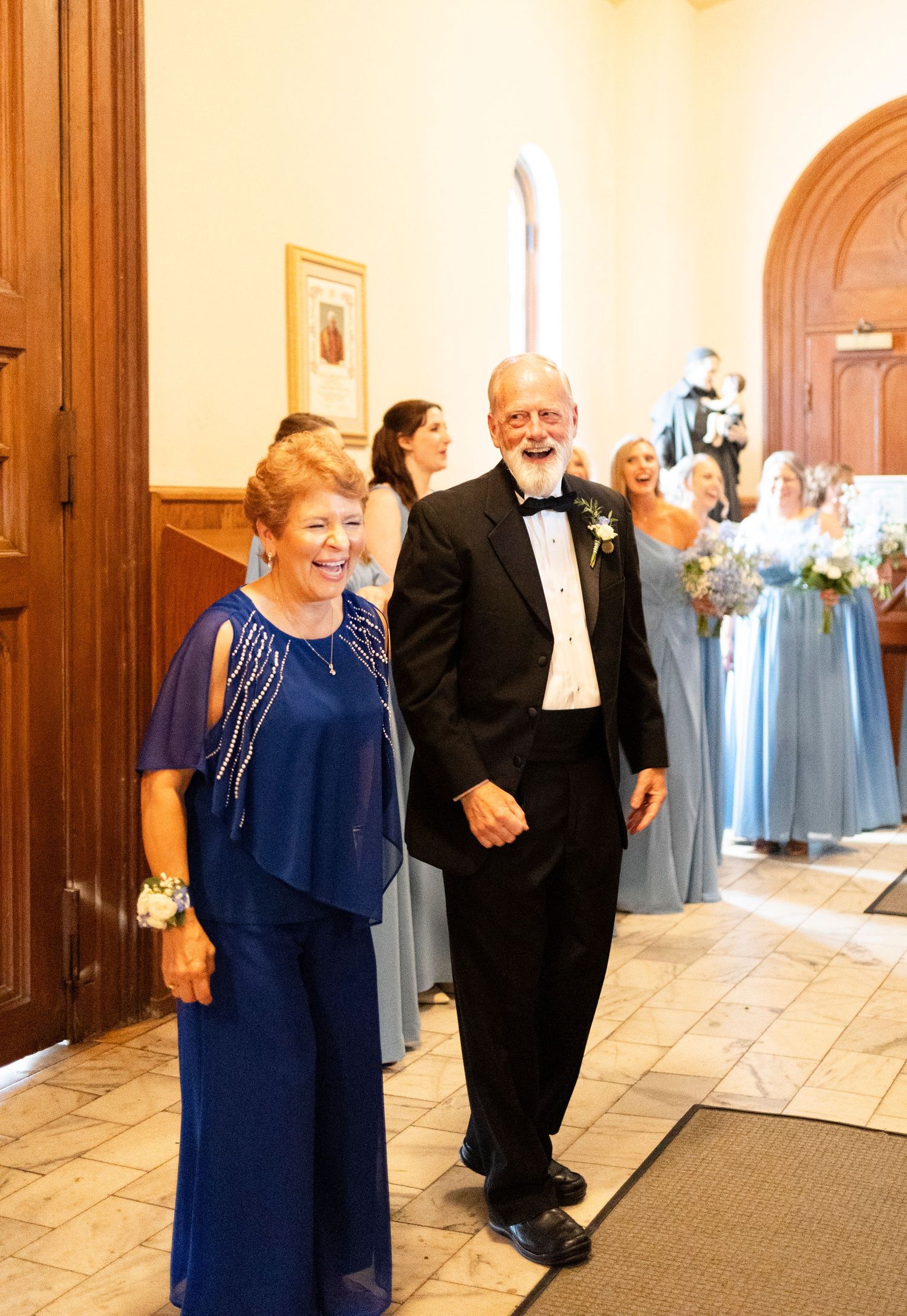 Elegant couple in navy attire walking down wedding aisle with bridesmaids in blue dresses in background at Catholic church in Augusta, GA.