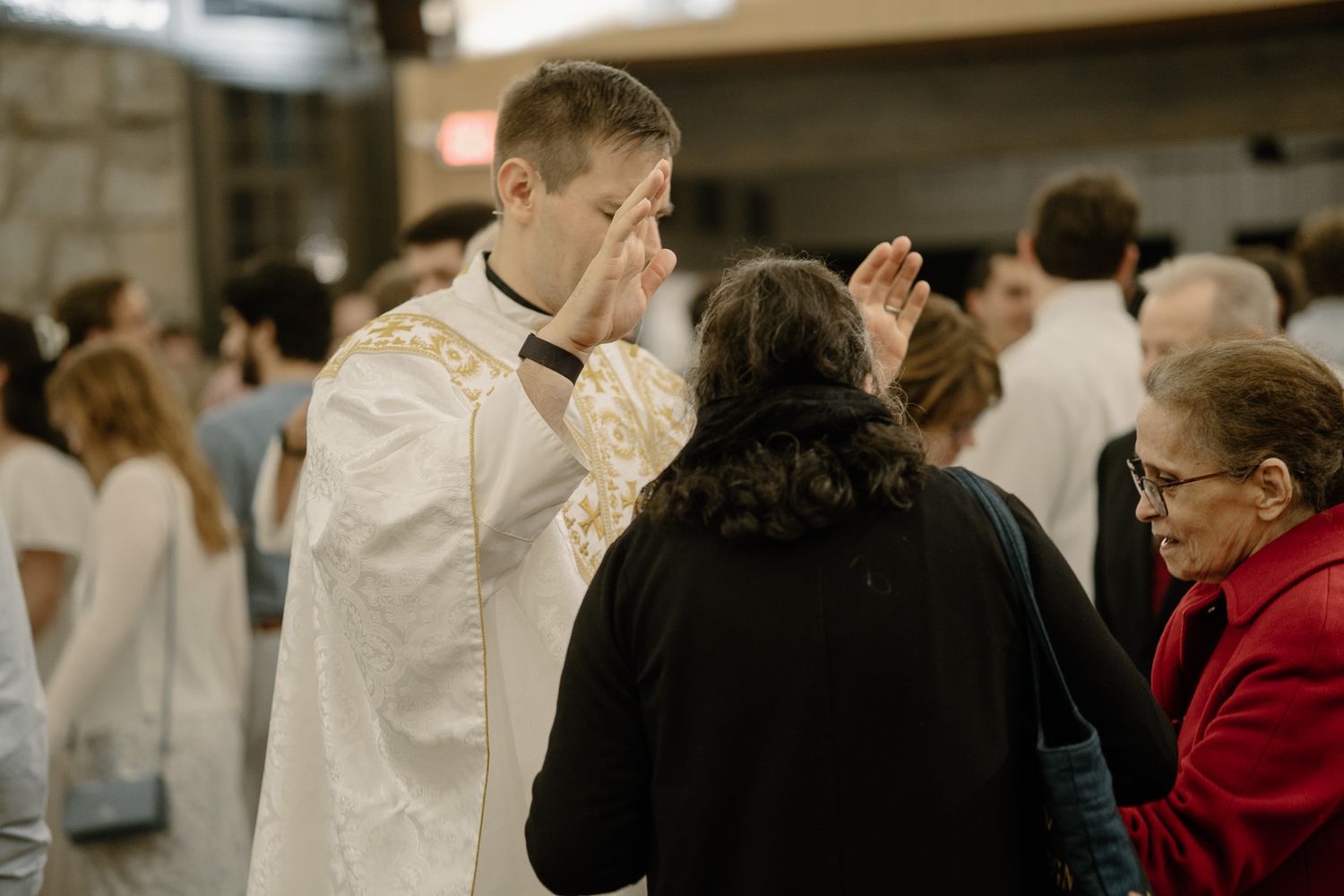 A priest in white vestments performs a blessing on parishioners during Catholic Mass in Athens, GA.
