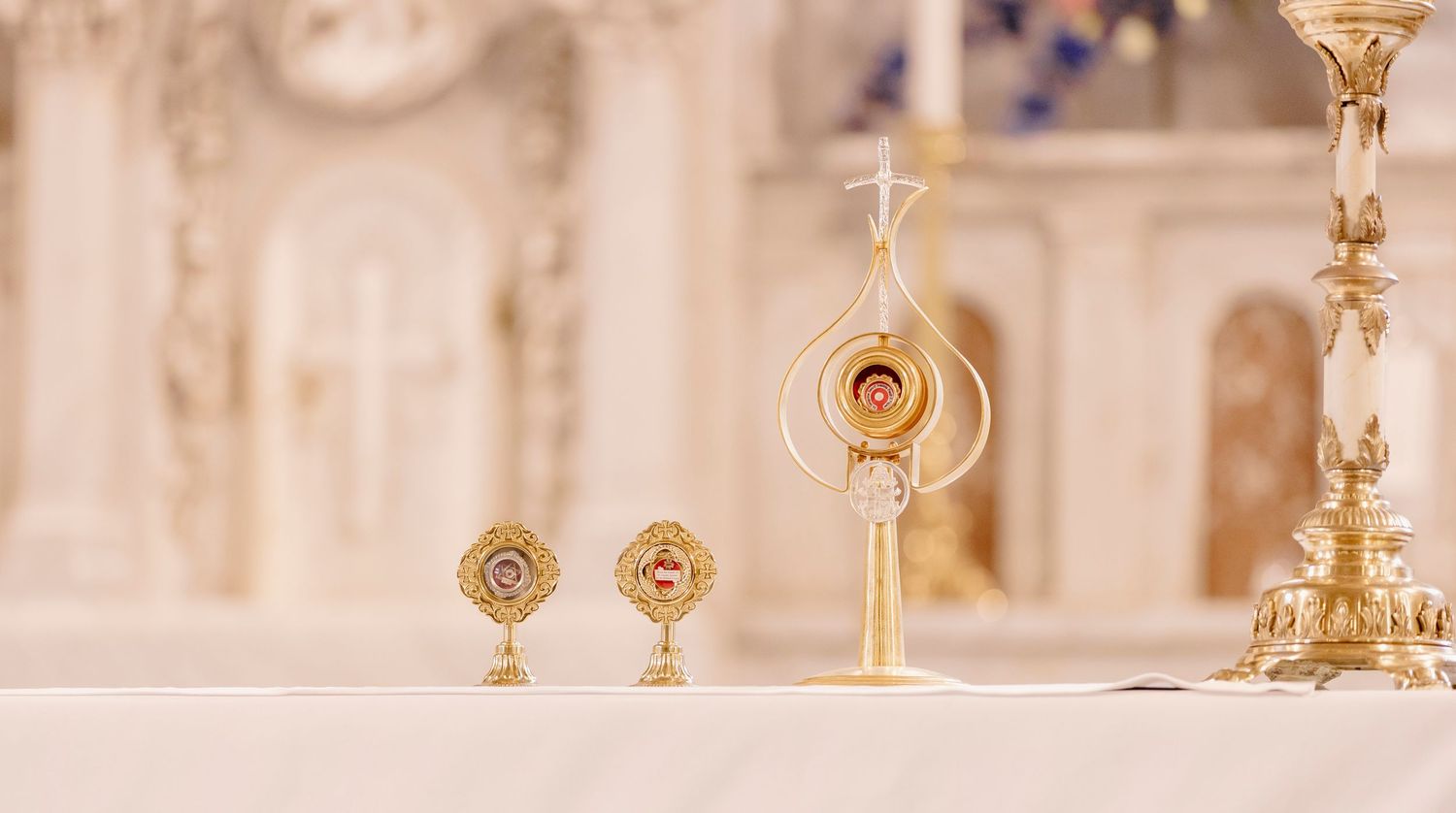 Golden Catholic reliquary and monstrance displayed on a white altar in an ornate church sanctuary.