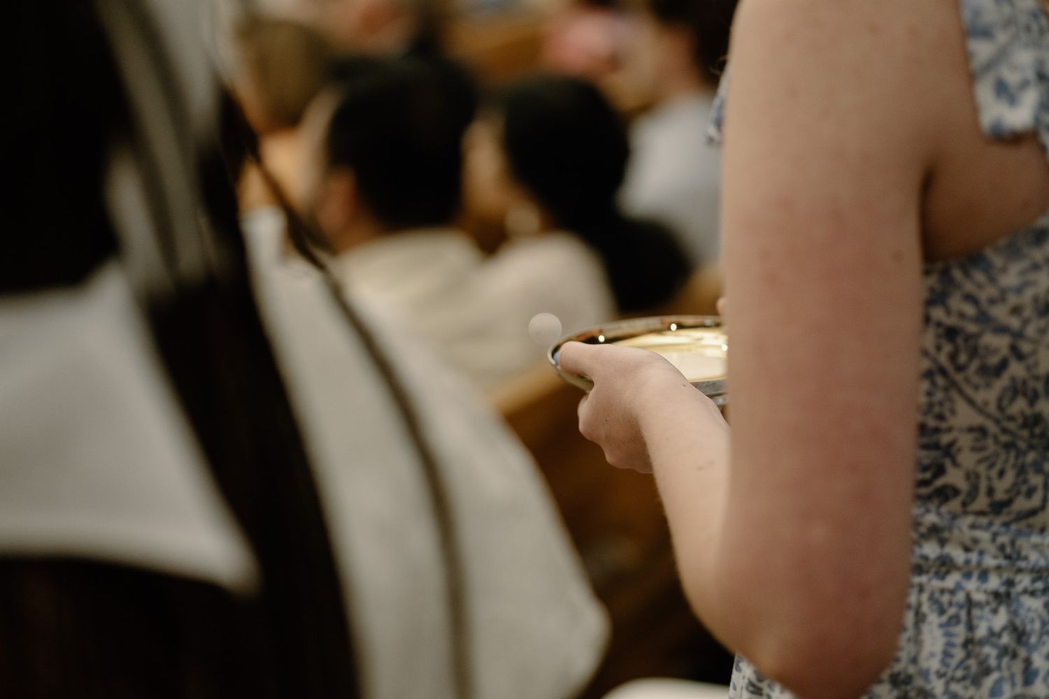 Woman holding communion paten during Catholic Mass with congregation seated in pews in background at UGA's Catholic Center.