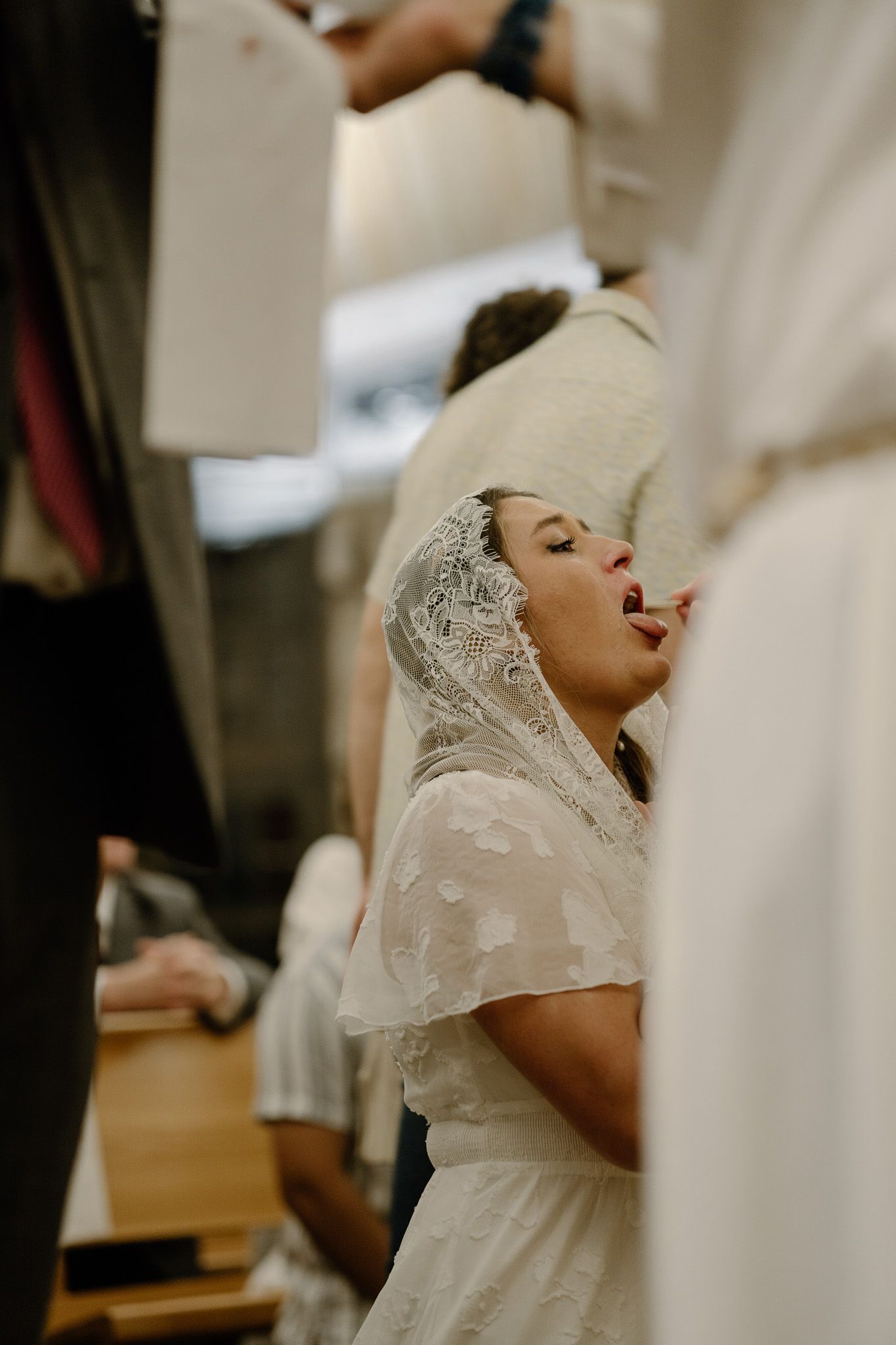 Woman in white lace veil receiving communion with eyes closed during a Catholic Mass in Athens, GA.