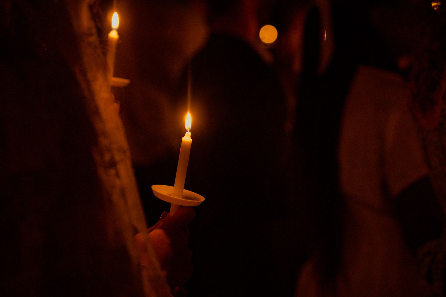 Hands holding lit candles in darkness during an Easter Vigil candlelight ceremony in Athens, GA.