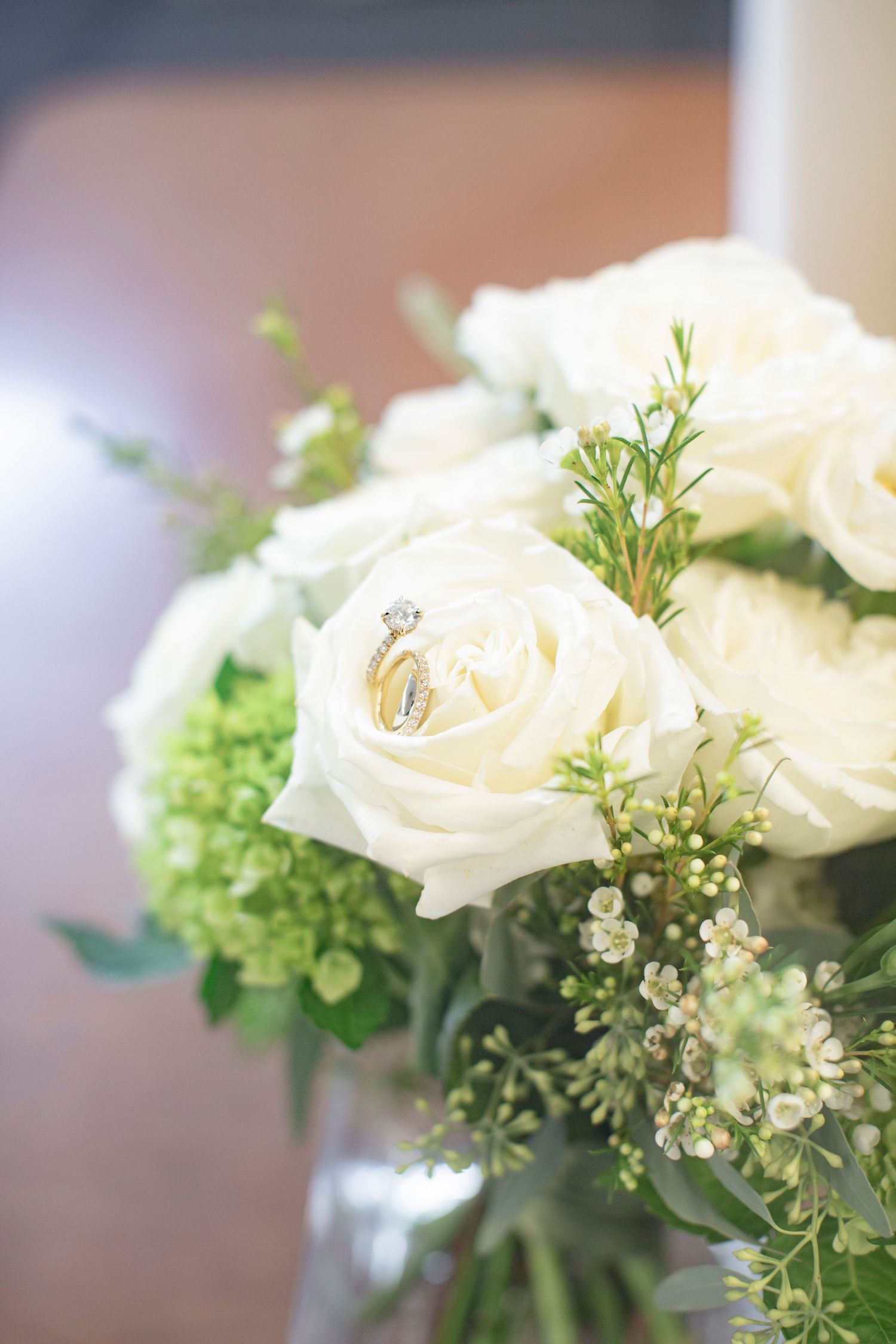 White rose bouquet with diamond engagement ring nestled among blooms and greenery, perfect for catholic wedding photography.